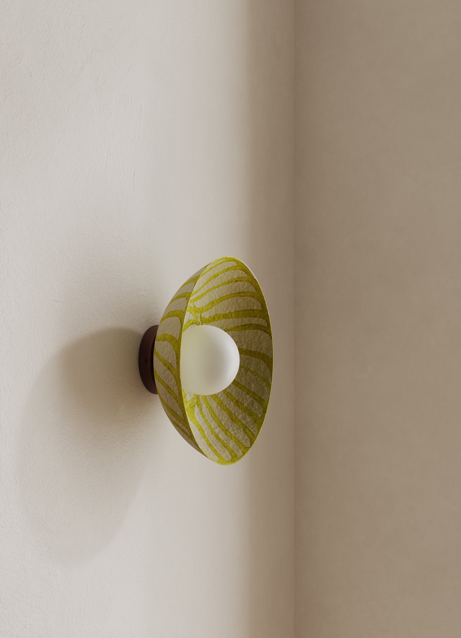 Wall-mounted light fixture with a patterned yellow shade on a neutral wall with brown backplate