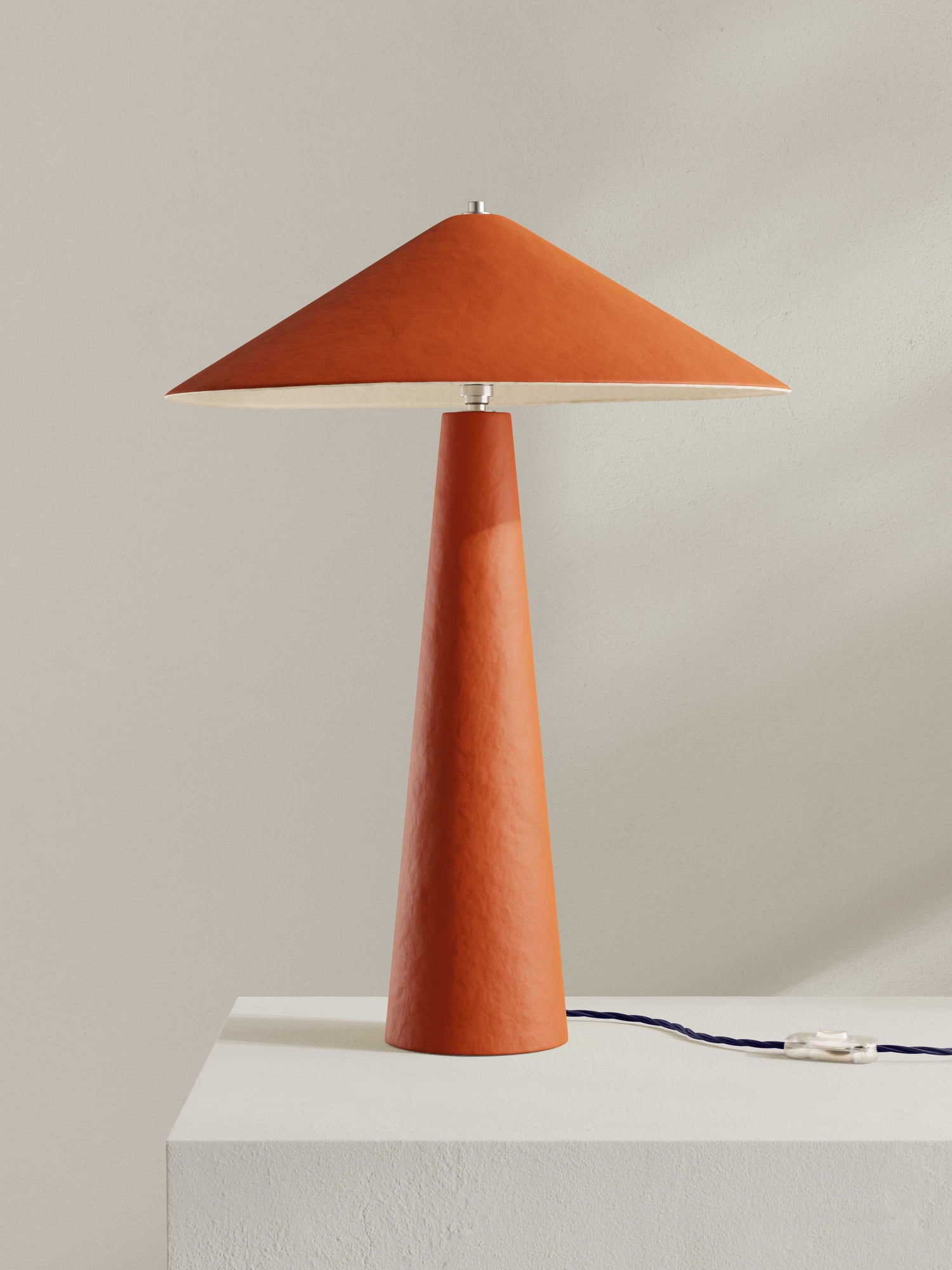 Parasol table lamp with tall stem and wide shade, made of hand-painted paper pulp in orange/red hue.