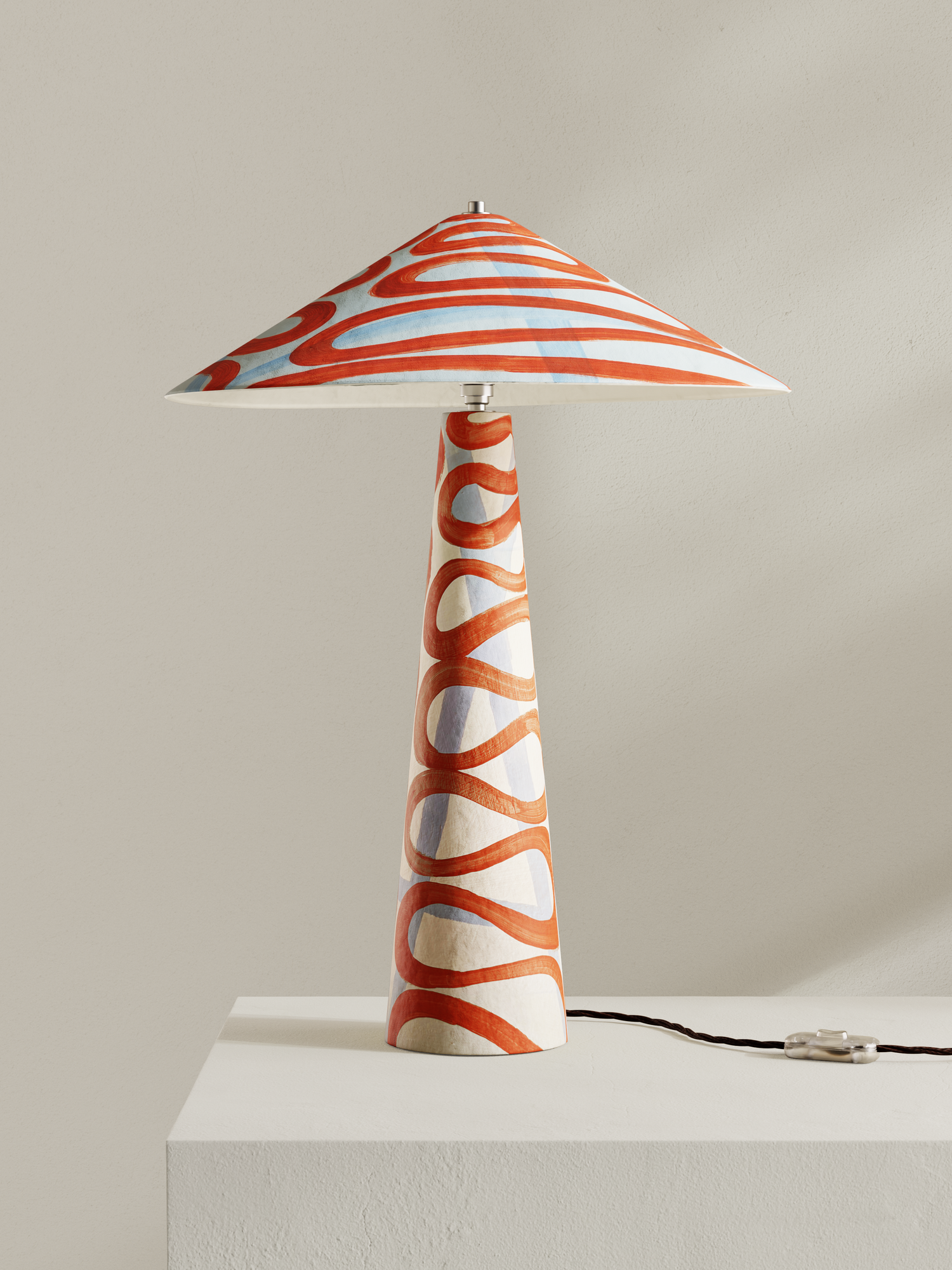 Parasol table lamp with tall stem and wide shade, made of hand-painted paper pulp in swirling orange/red Serpent pattern