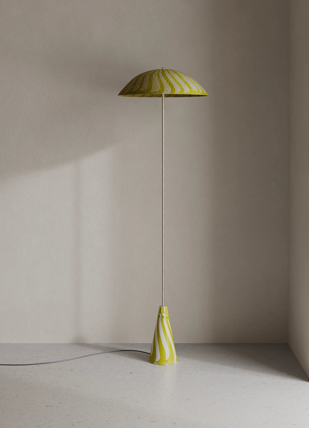 A modern floor lamp with a yellow and white shade and matching base, standing on a light gray floor against a beige wall.