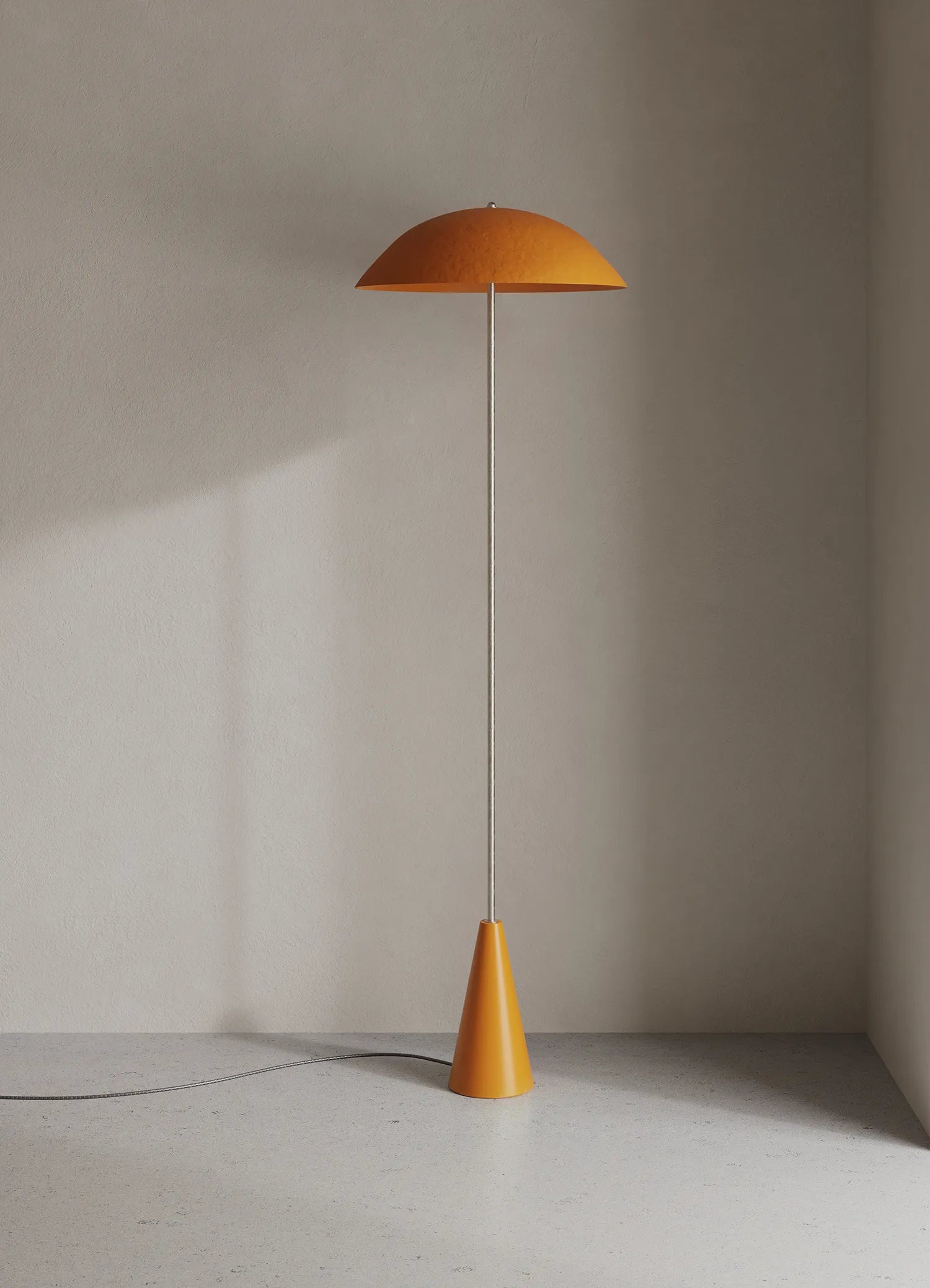 A modern floor lamp with a wide, dome-shaped orange shade and a tapered orange base, standing on a light gray floor against a textured beige wall.