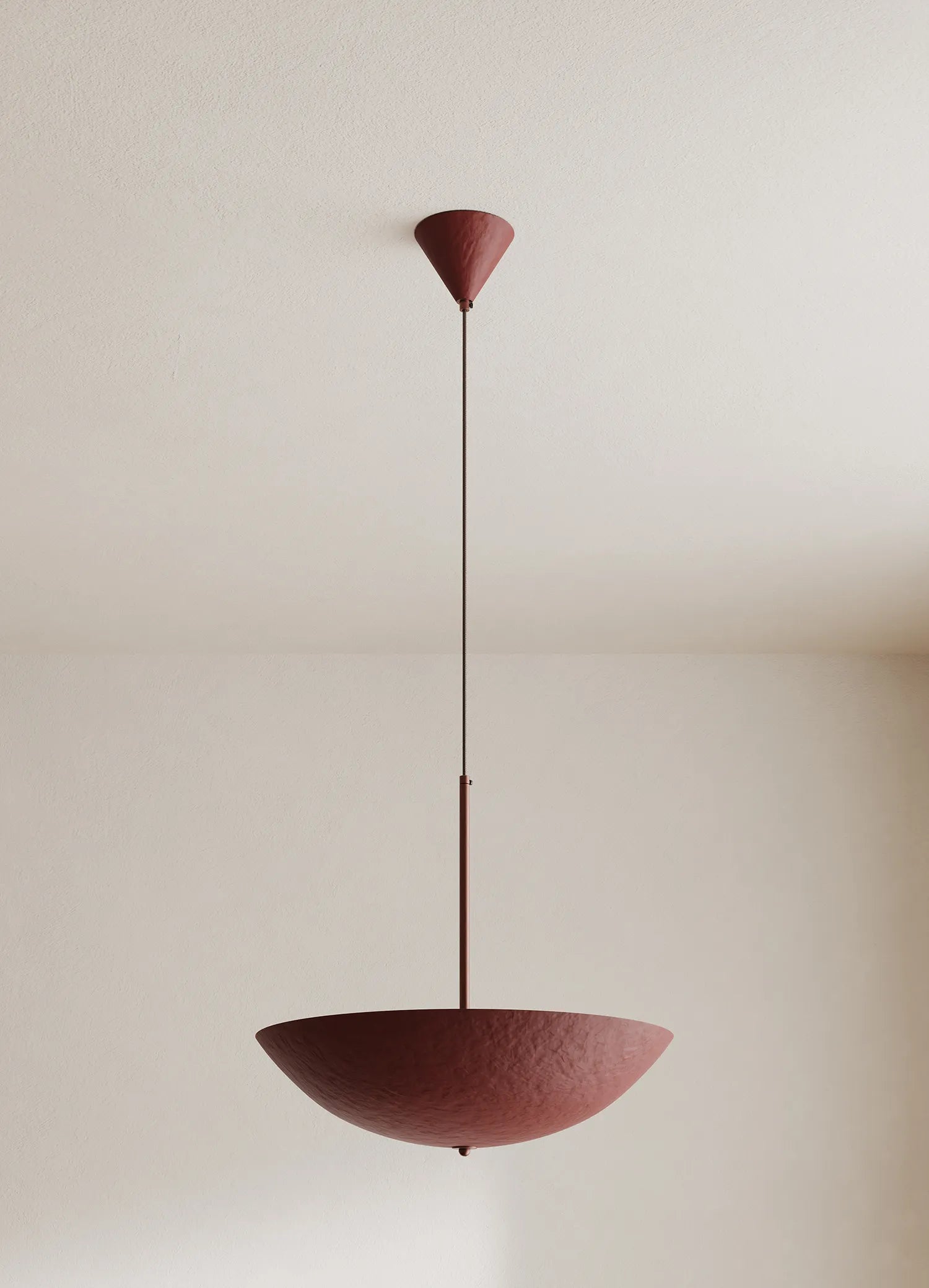 A modern pendant light with a textured deep red-colored bowl shade and matching ceiling canopy, suspended by a thin rod against a neutral off-white wall.