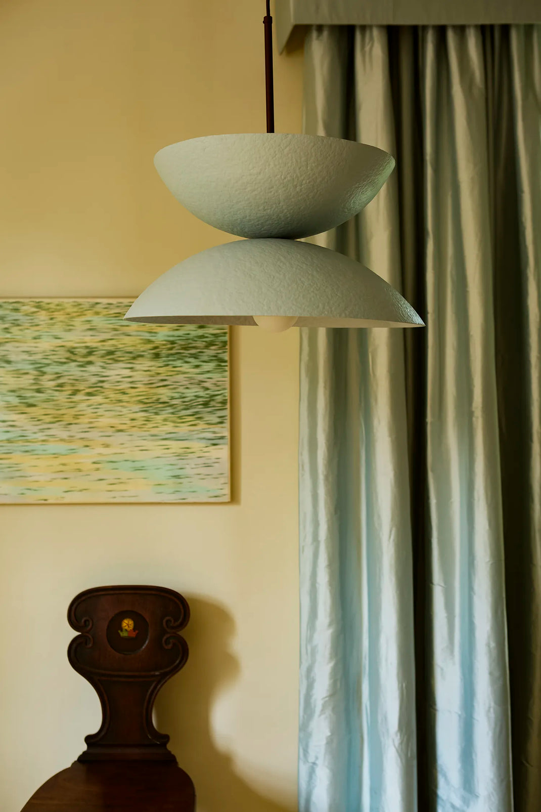 Light blue pendant lamp hanging in a room with a painting and curtains.