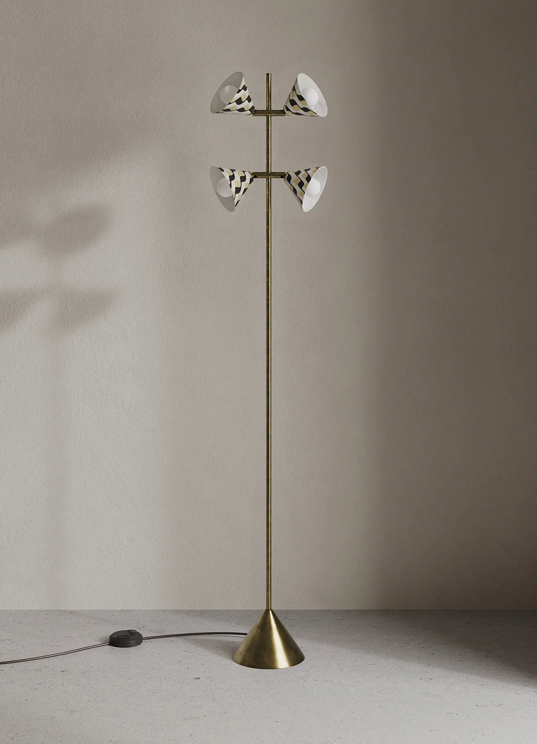 A tall brass floor lamp with four white and black patterned shades, standing on a concrete floor against a neutral beige wall.
