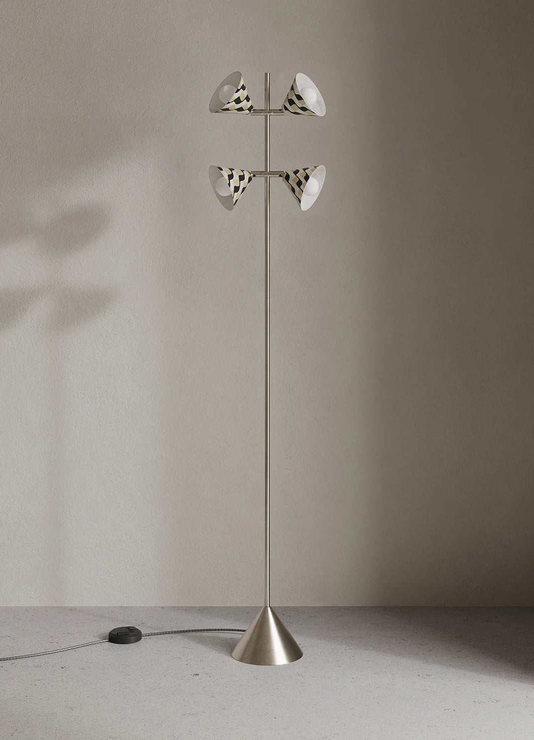 A modern floor lamp with a slim metallic base and two tiers of cone-shaped white shades with black stripes, set against a minimalist beige wall.