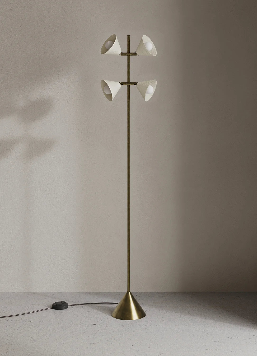A modern floor lamp with a slim brass-colored metal stand, a conical base, and four white bell-shaped glass shades arranged in two pairs, set against a minimalist beige wall and floor.