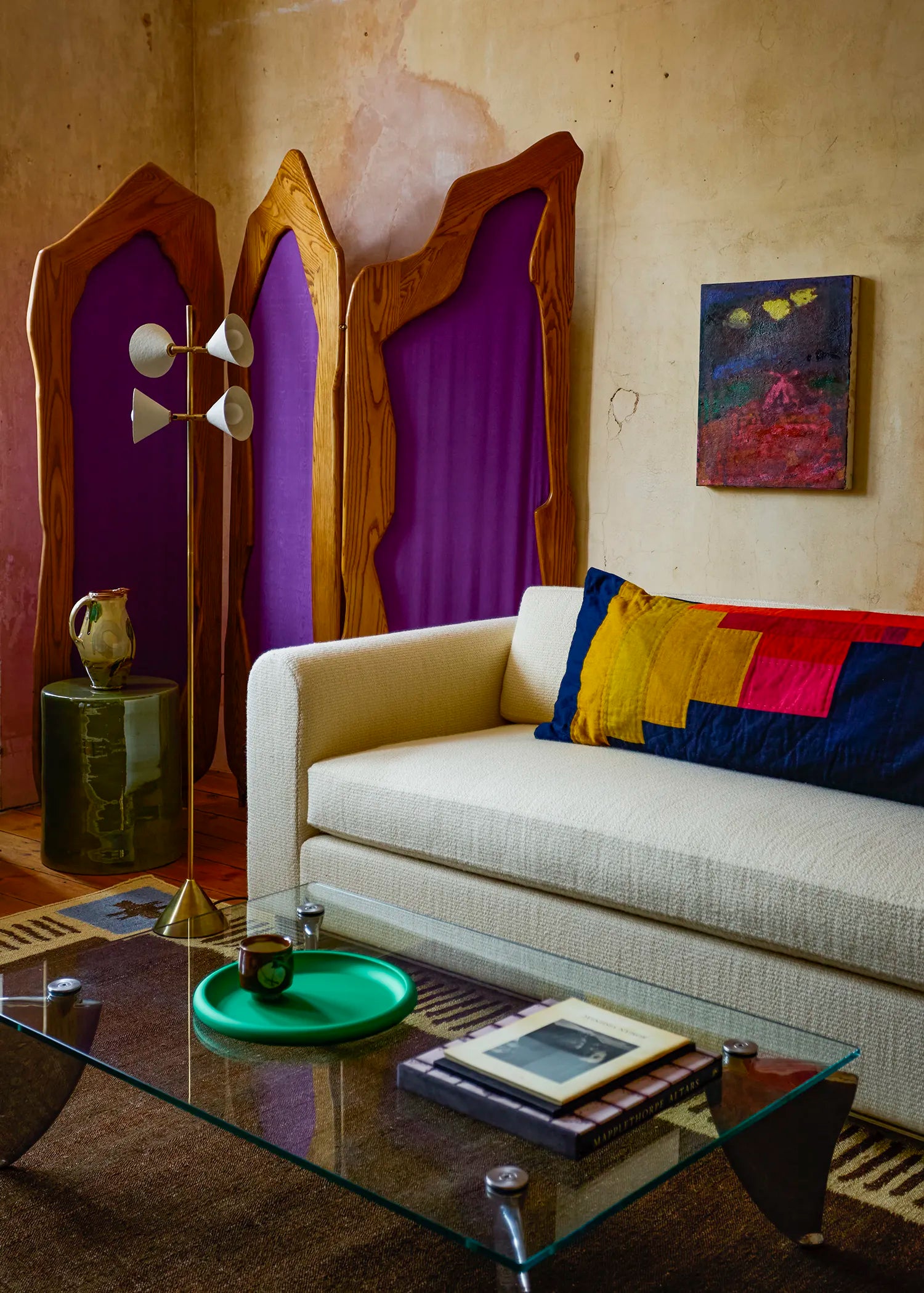 A cream-colored textured sofa in a retro-styled living room, featuring a floor lamp with four white shades in front of a purple and wood arched tri-fold screen.