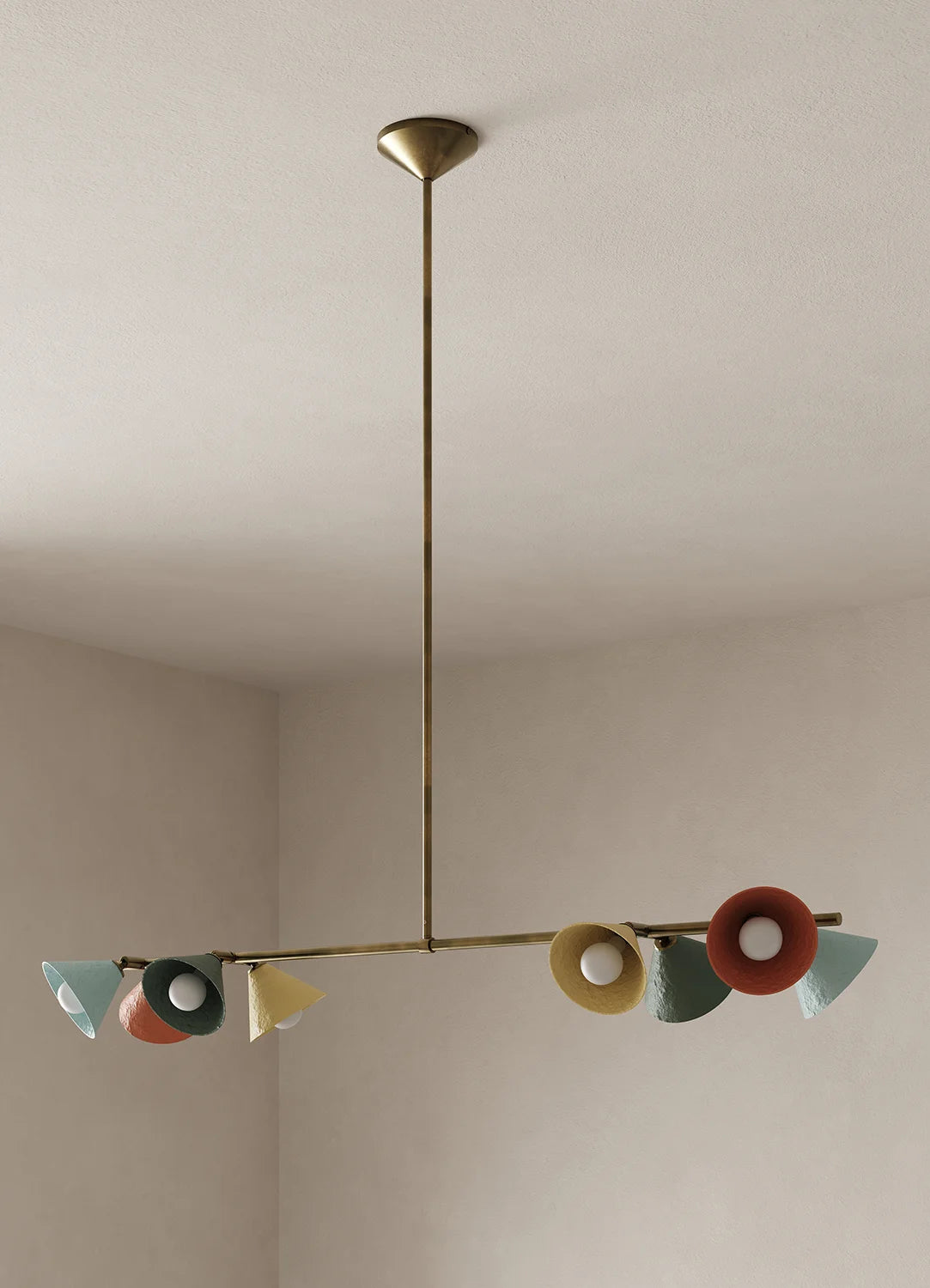 A modern brass chandelier with multiple colorful lights in shades of blue, green, yellow, and terracotta, suspended from a ceiling in a minimalist room.