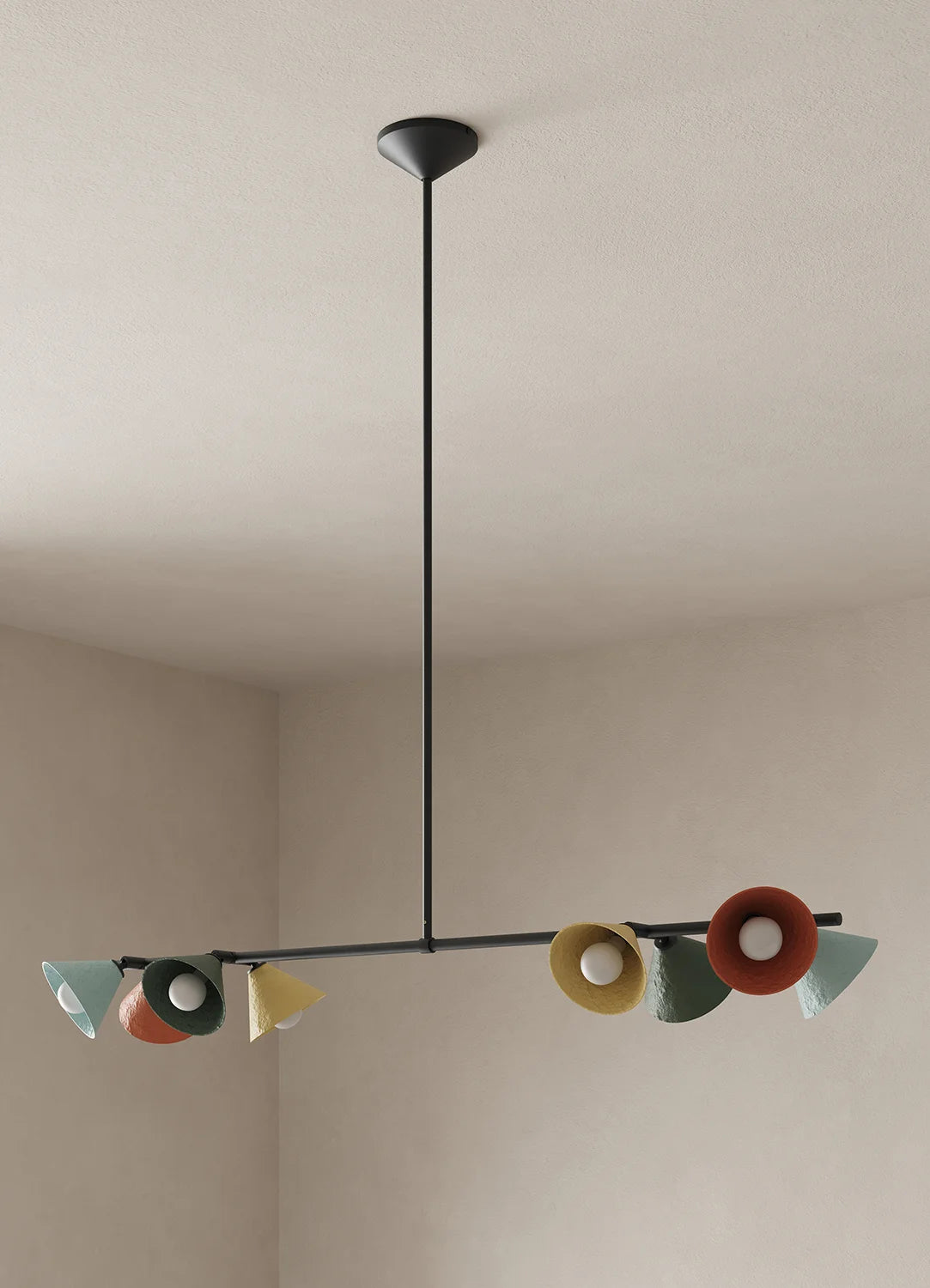A modern multi-light linear chandelier with a black metal frame and multiple colorful, sculptural shades in terracotta, yellow, green, and mint, suspended from a ceiling in a minimalist room.