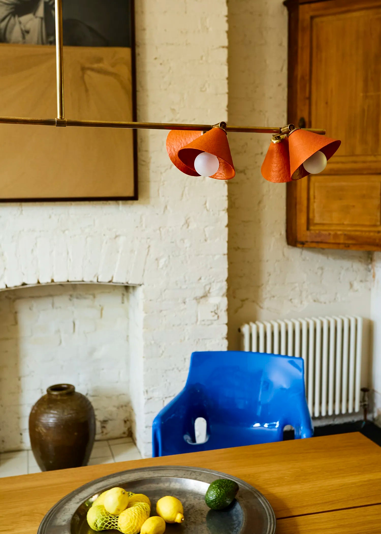 Palefire Studio Garland pendant light in antique brass with brick-red cone shades, shown above a wooden dining table with a blue chair.