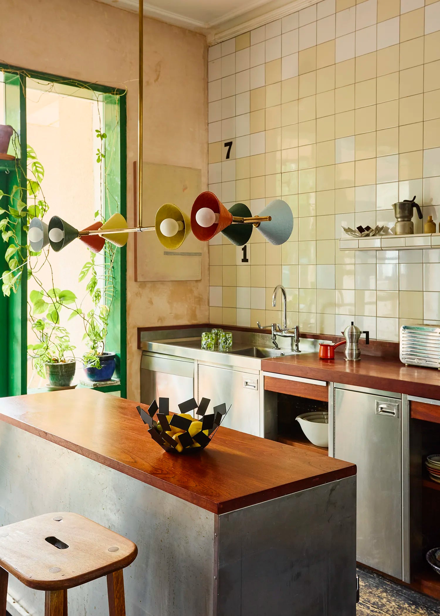 Palefire Studio Garland pendant light in antique brass with multicoloured cone shades, suspended above a kitchen island in a colourful tiled interior.