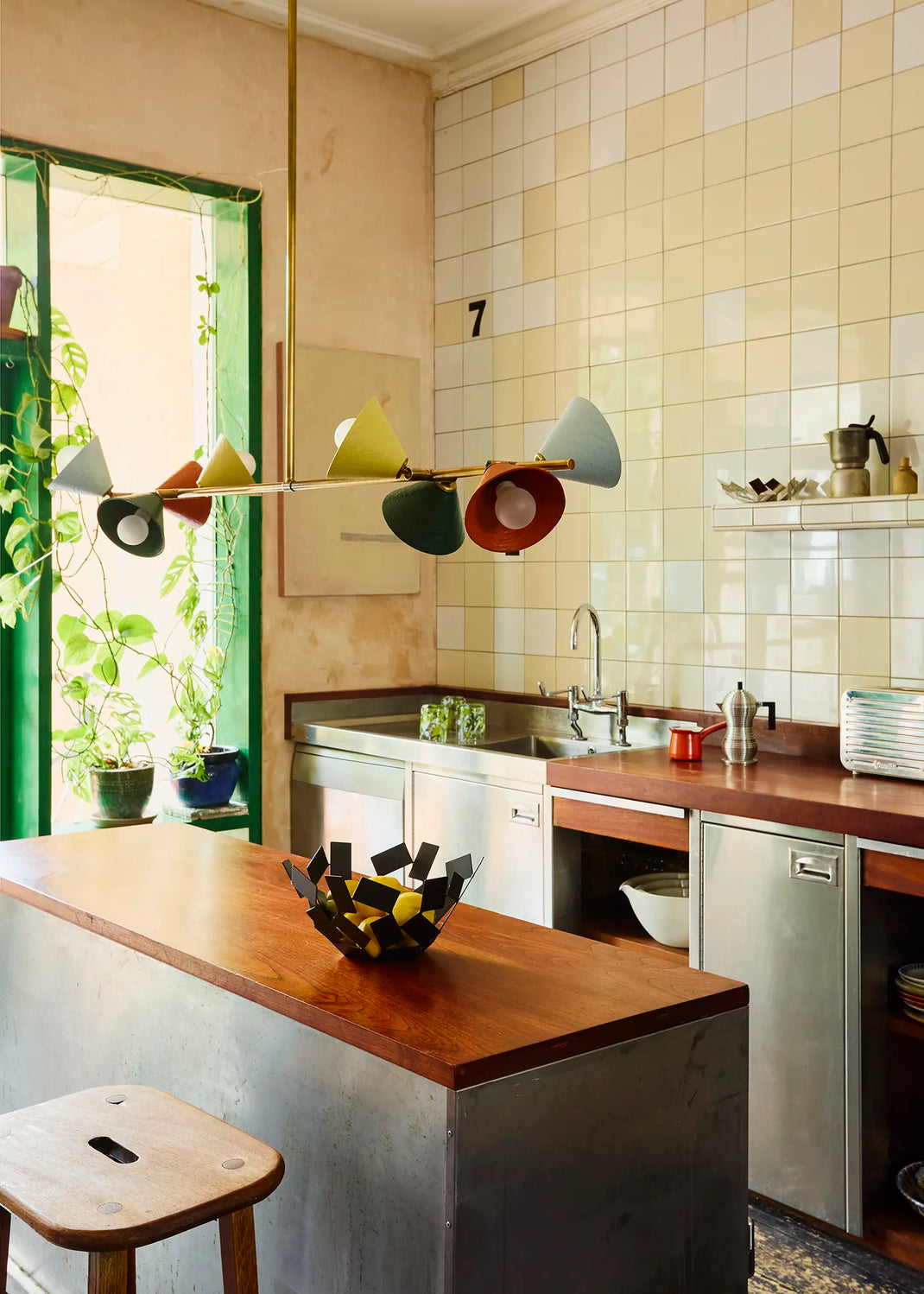 Modern kitchen interior with Palefire Studio Garland pendant light in antique brass with multicoloured cone shades, suspended above a kitchen island in a colourful tiled interior.