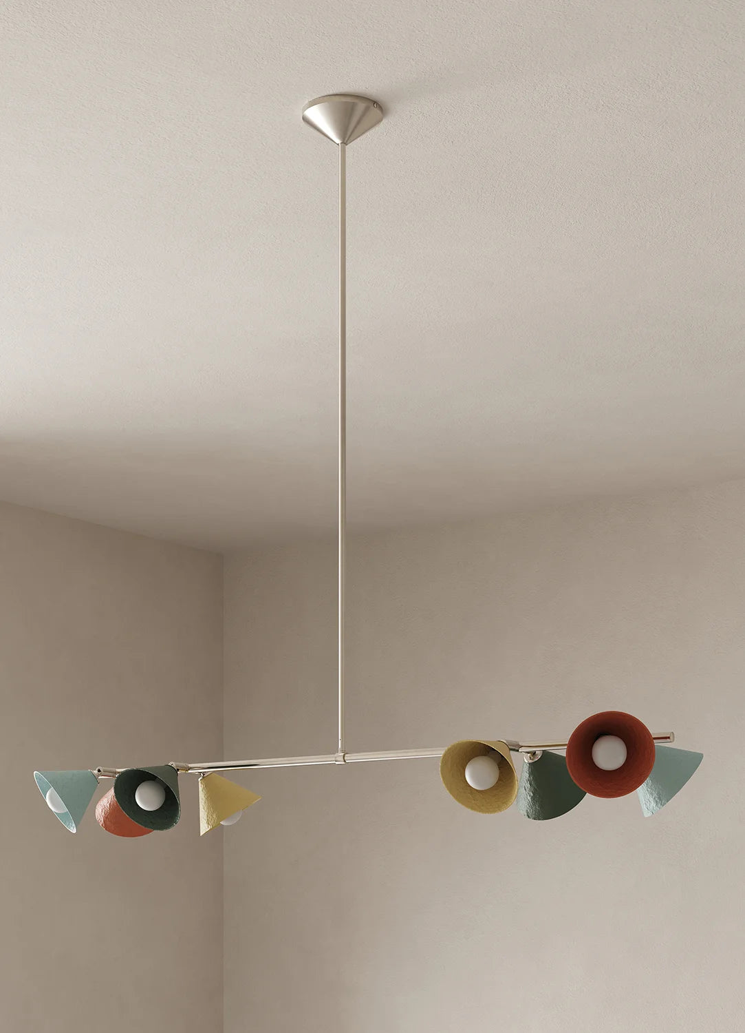 A modern multi-light linear chandelier with colorful cone shades in blue, green, yellow, and terracotta, suspended from a polished nickel ceiling canopy in a minimalist room.