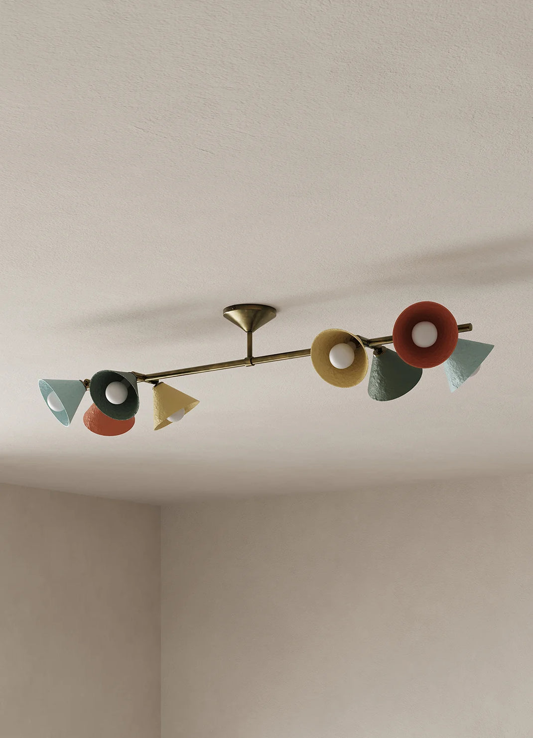 A mid-century modern ceiling light fixture with a brass-toned horizontal bar and multiple colorful shades in red, yellow, green, and blue, mounted on a textured off-white ceiling.