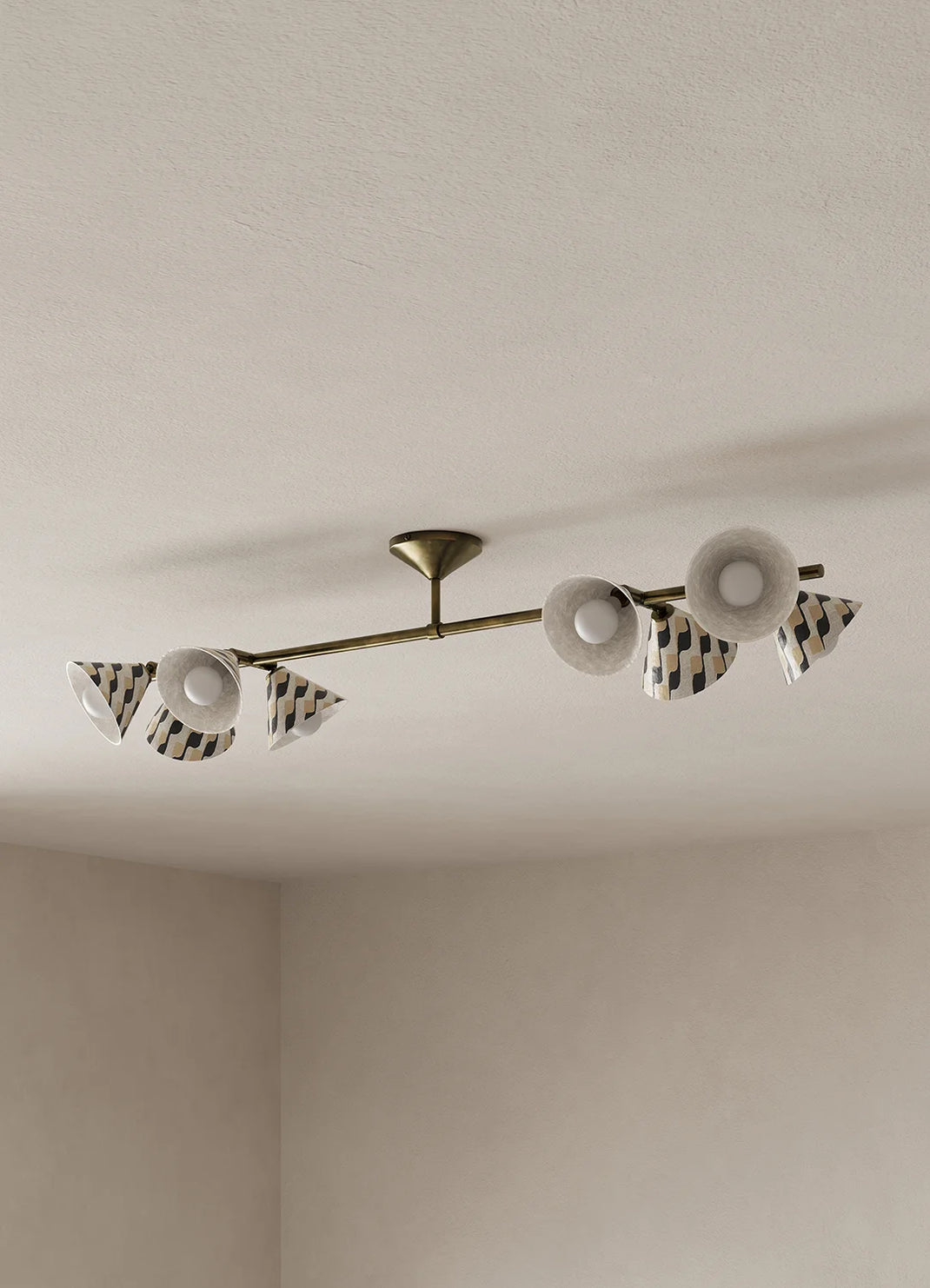A modern ceiling light fixture with a brass-toned horizontal bar, featuring eight white and black patterned cone shades mounted on a textured off-white ceiling.