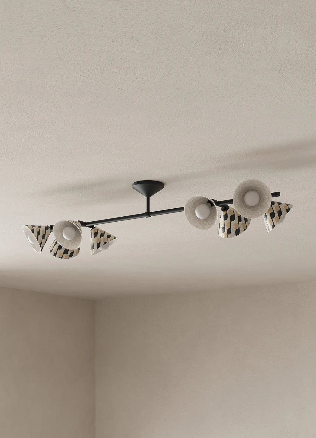 A modern ceiling-mounted light fixture with a black horizontal bar and multiple white and black patterned shades, installed on a textured off-white ceiling in a minimalist room.