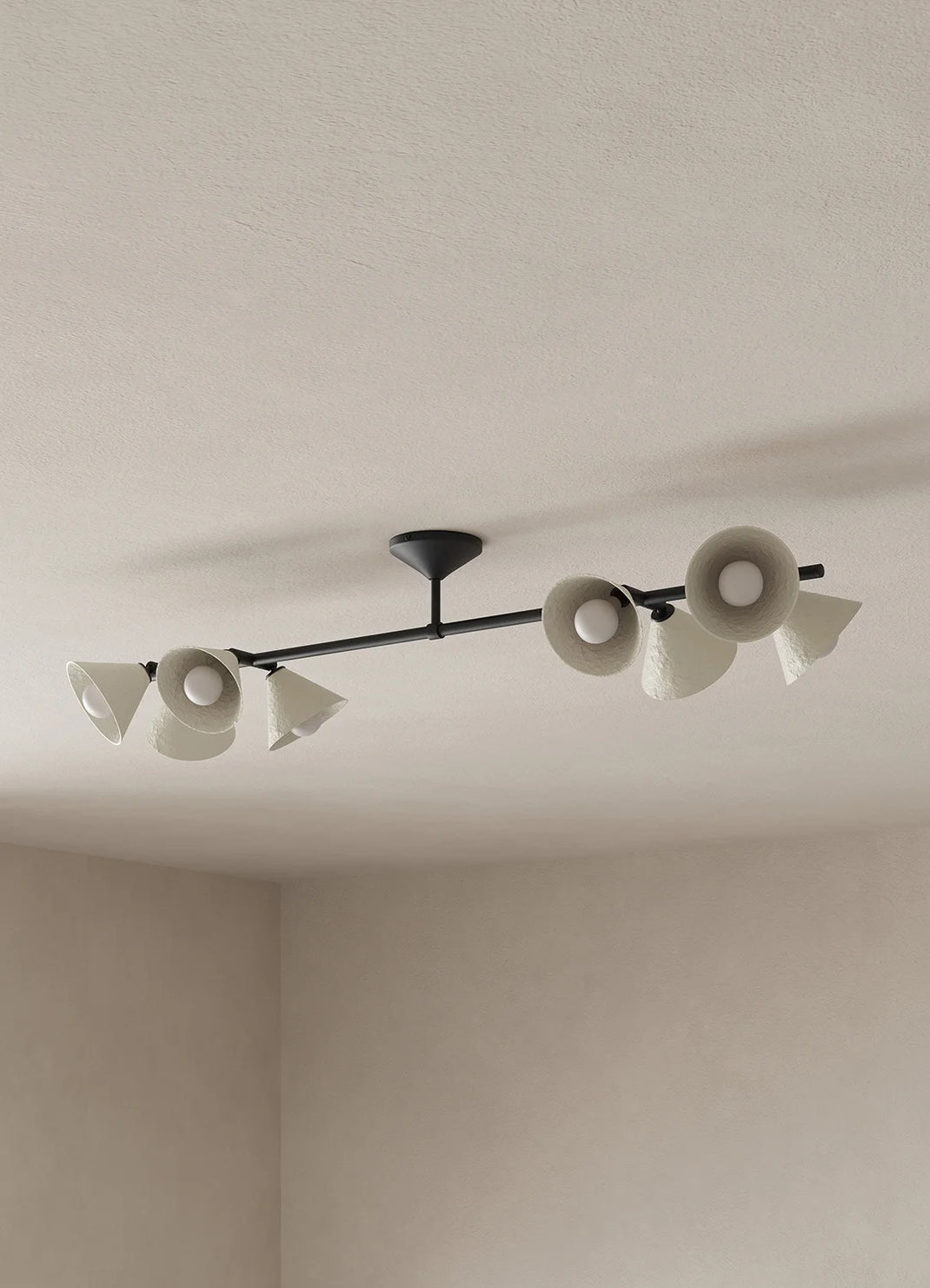 A long, surface mount light with black metalware and eight off-white shades hangs from a ceiling against a neutral background