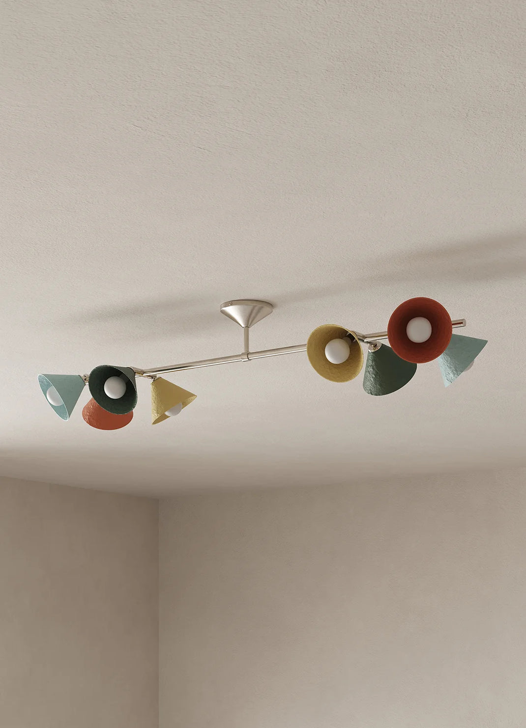 A mid-century modern linear ceiling light fixture with multiple colorful cone-shaped shades in red, yellow, green, and blue, mounted on a ceiling in a neutral-toned room.