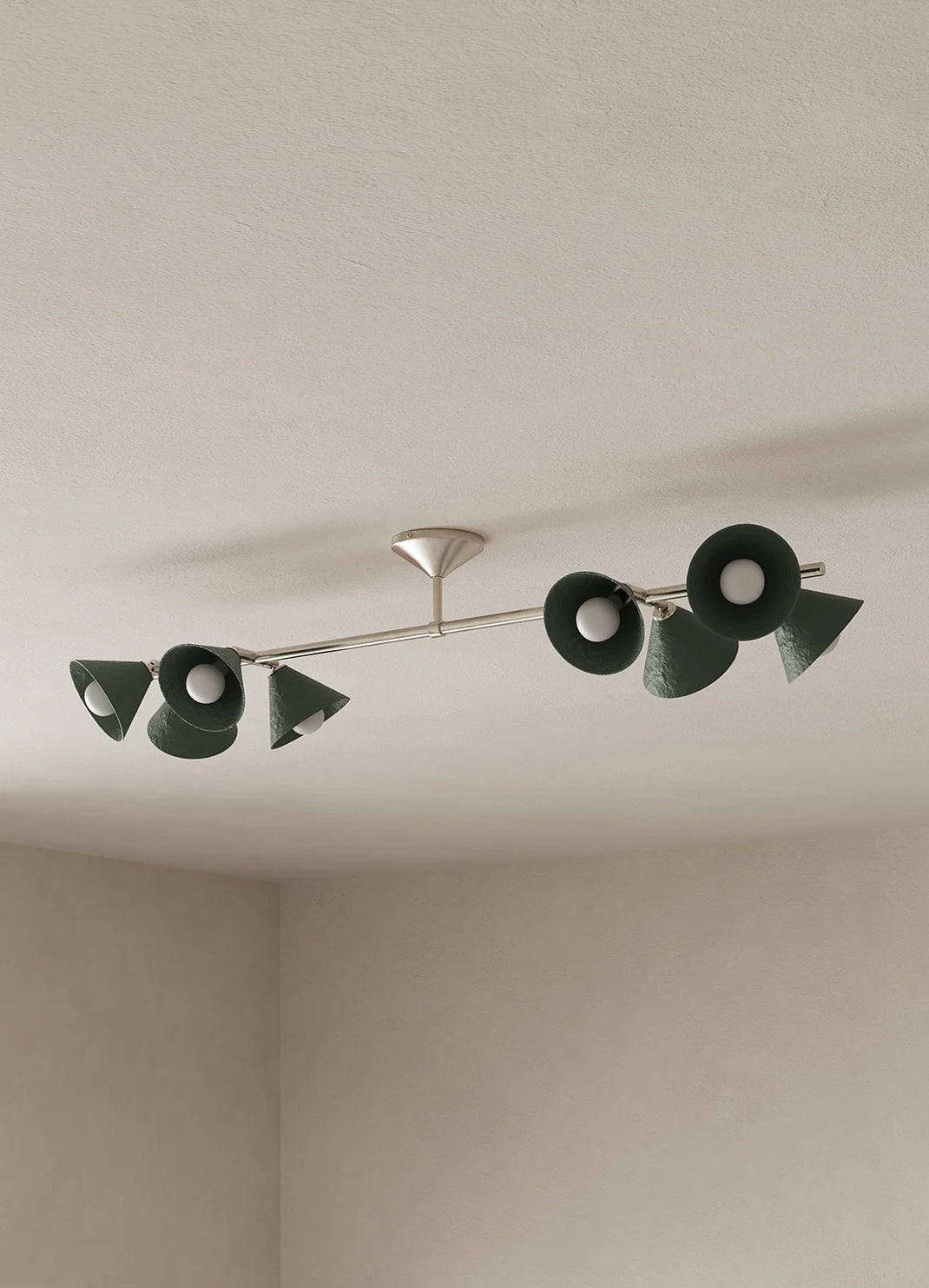 A modern ceiling-mounted light fixture with eight dark green cone-shaped shades and a silver metal arm, installed on a textured off-white ceiling.