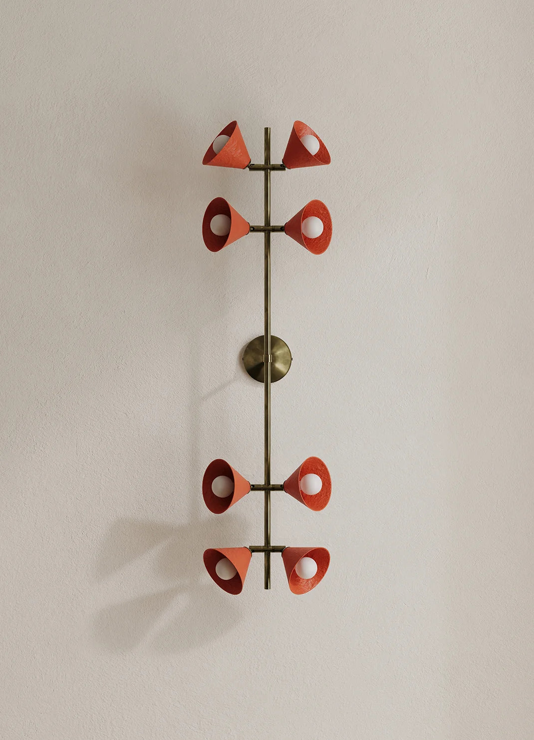 A mid-century modern wall sconce featuring a vertical bronze-finished metal frame with eight red-orange cone-shaped shades arranged symmetrically, mounted on a plain beige wall.