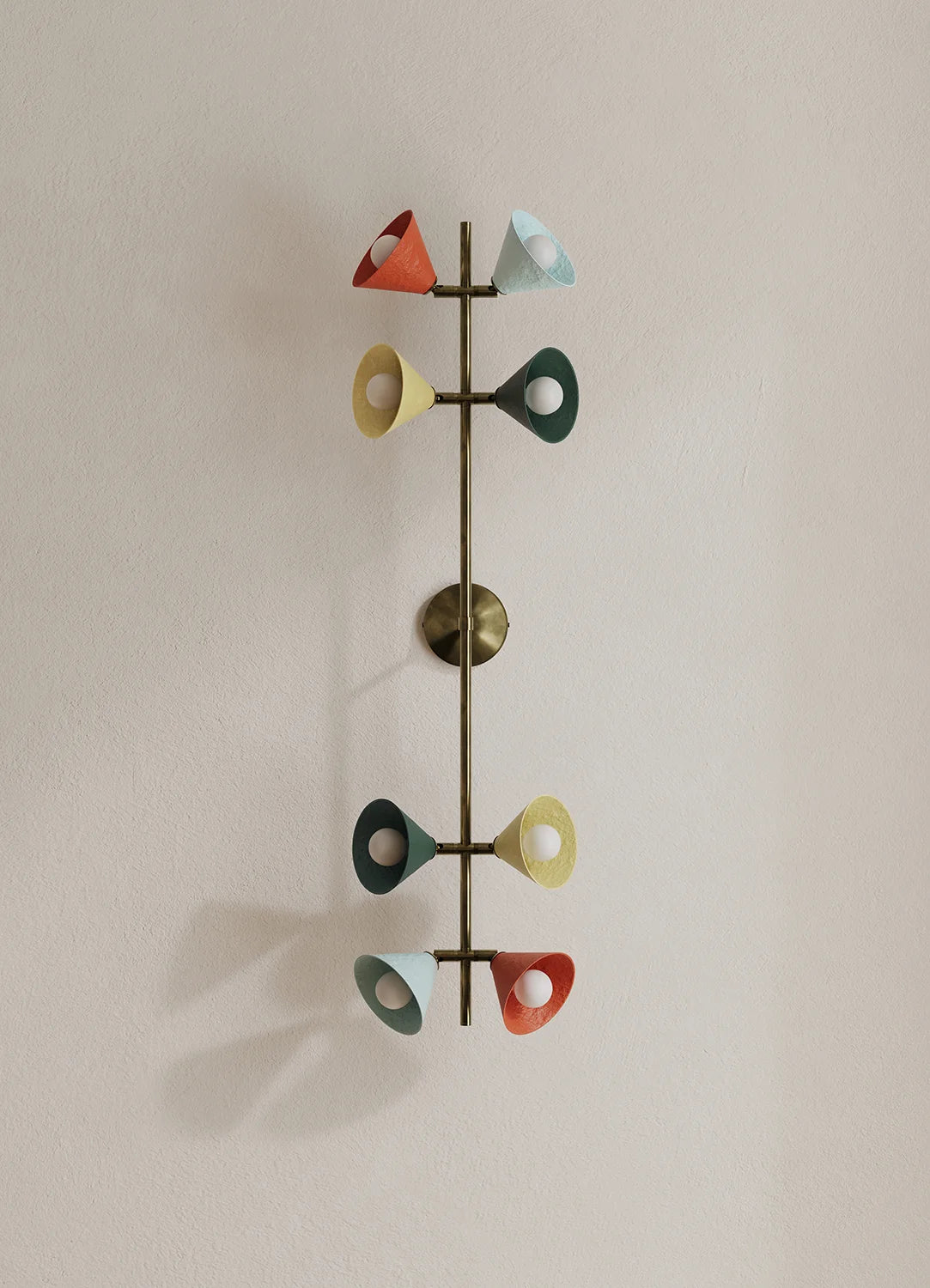 A mid-century modern wall sconce with a vertical bronze-finished metal rod and multiple colorful cone-shaped shades in red, light blue, yellow, and dark green, mounted on a plain beige wall.