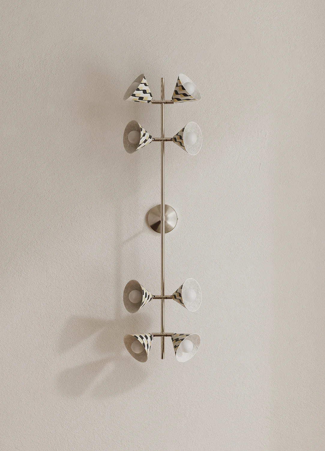 A modern wall-mounted light fixture with a vertical polished metal rod and eight angled lamp shades, some patterned with black and white stripes mounted on a beige wall.