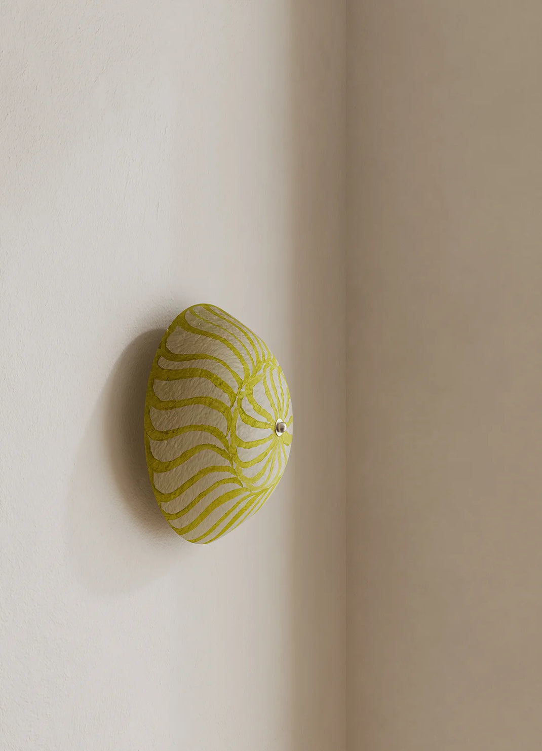 A modern wall-mounted sconce with a textured, yellow and white design, mounted on a warm beige wall corner.