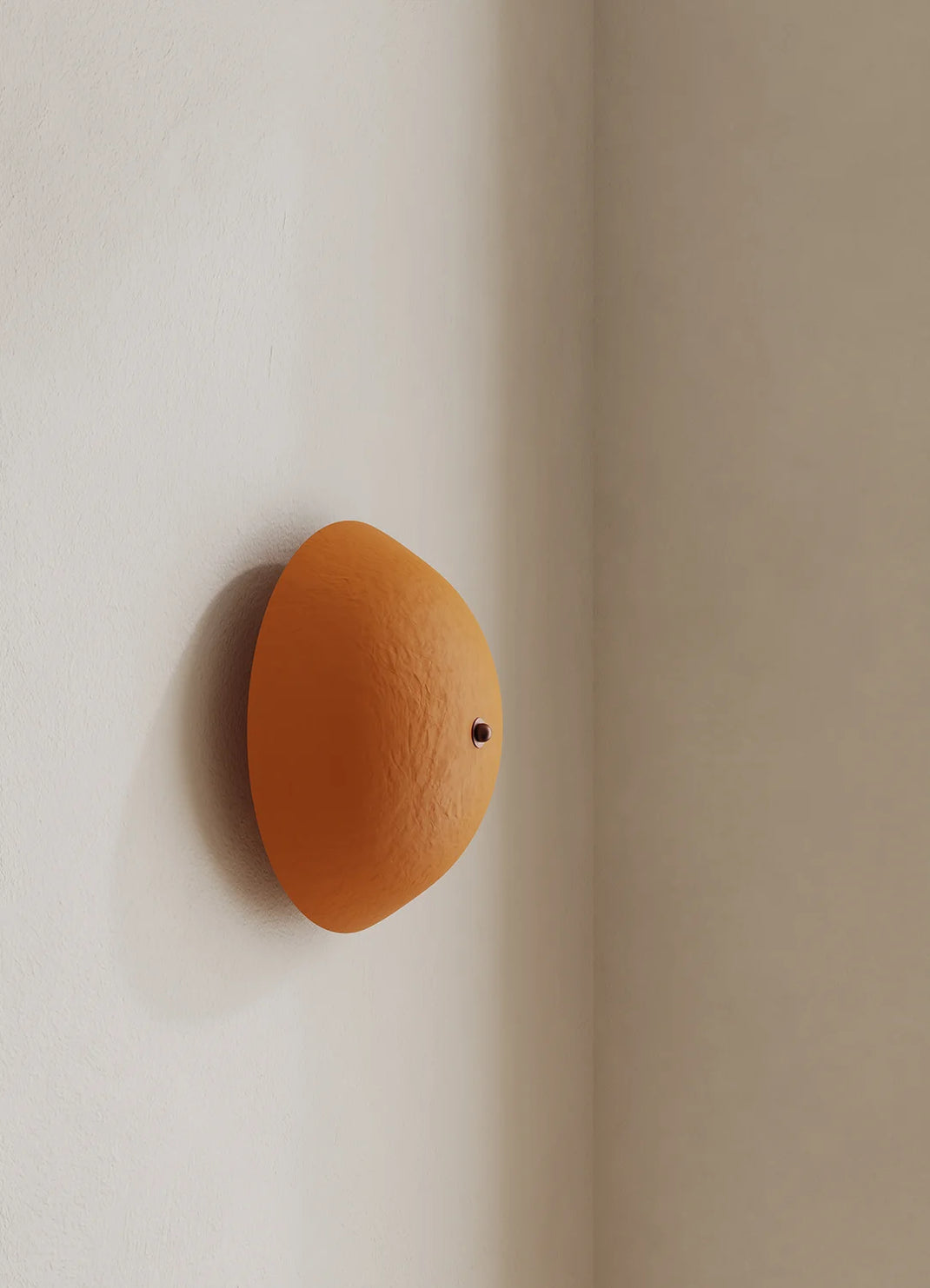 An dome-shaped wall sconce mounted on a warm beige corner wall, casting a soft shadow.