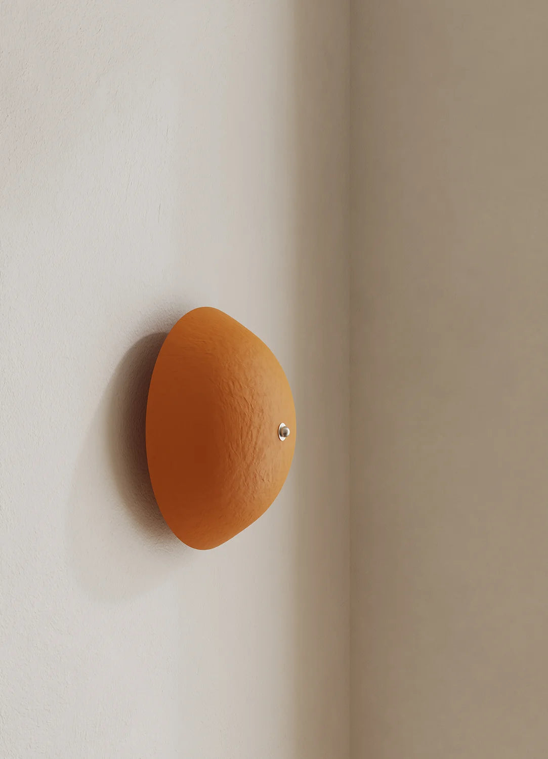 A dome-shaped wall sconce painted in orange mounted on a beige wall corner, casting a soft shadow.