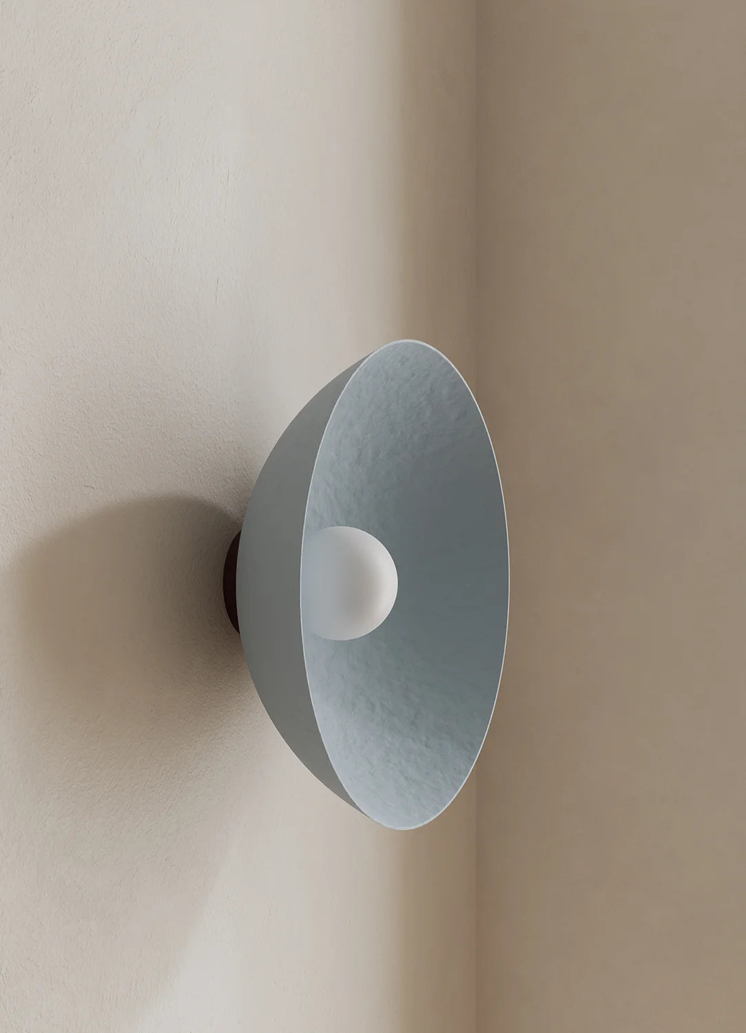 A modern wall-mounted light fixture with a wide, shallow dome shade in a muted blue finish and a white spherical bulb or diffuser at the center, shown mounted on a beige wall in an interior corner.