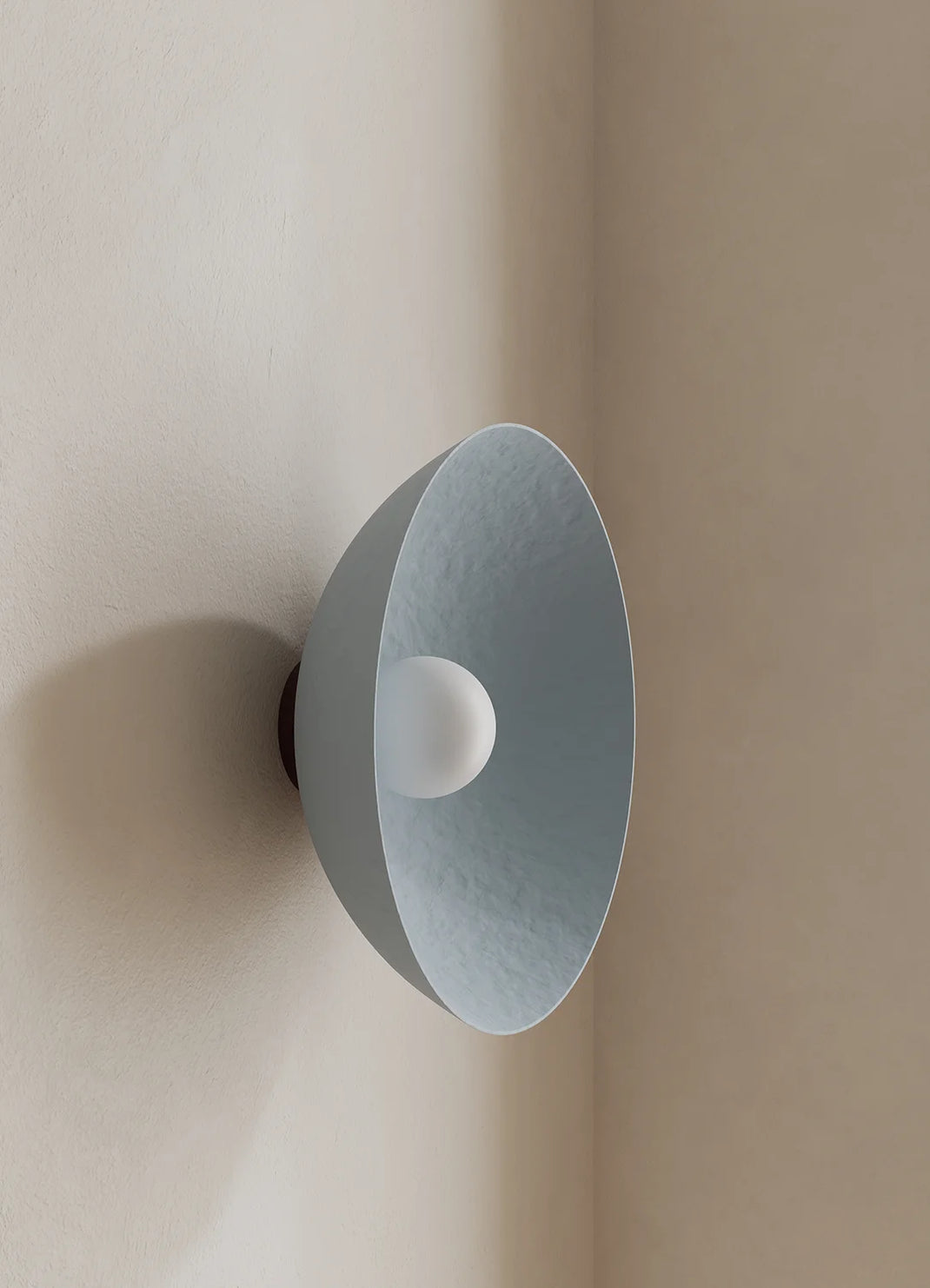 A modern wall-mounted light fixture with a wide, shallow dome shade in a muted blue finish and a white spherical bulb or diffuser at the center, shown mounted on a beige wall in an interior corner.
