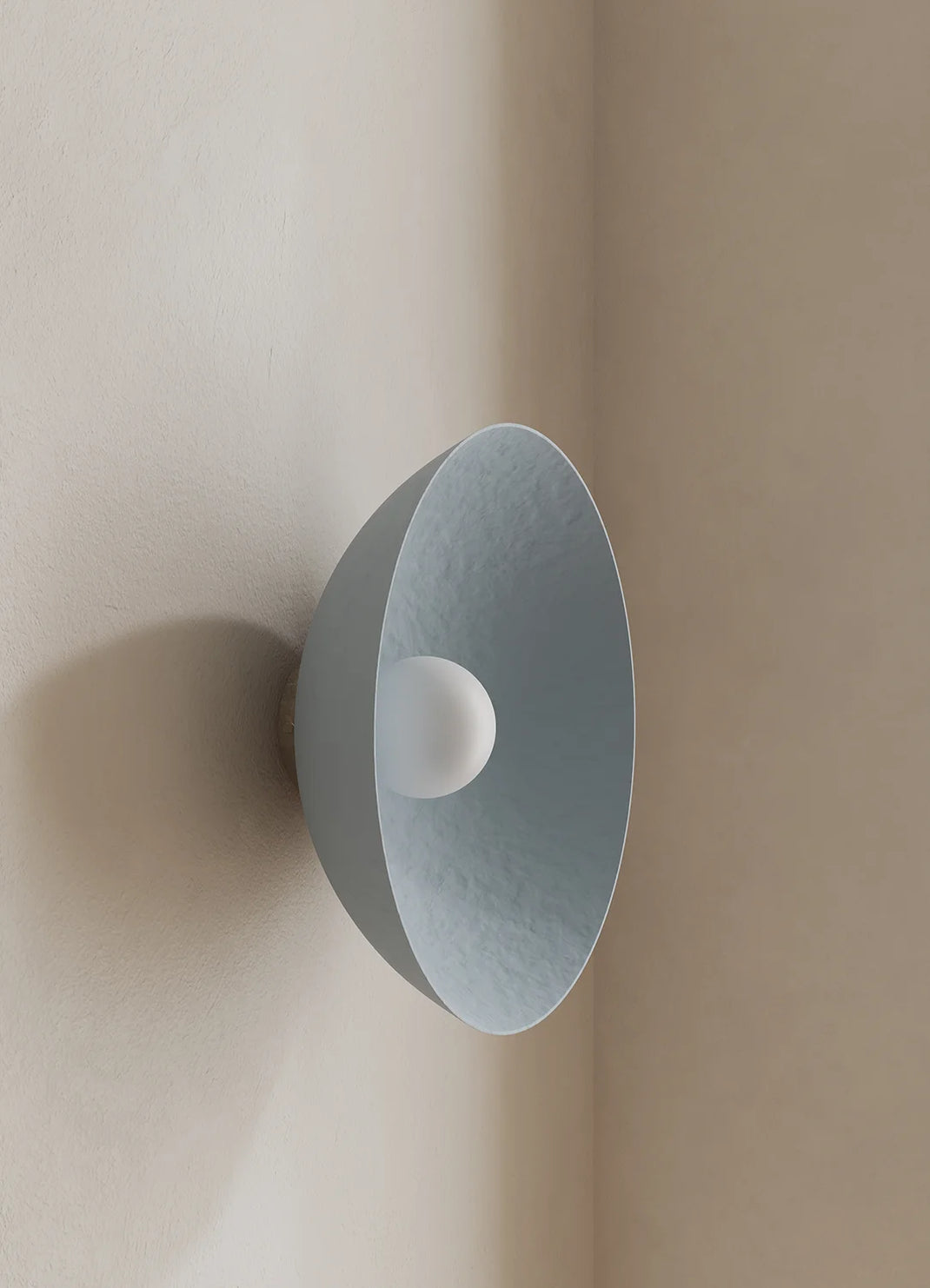 A modern dome-shaped wall sconce in a muted blue finish with a white bulb, mounted on a beige plaster wall corner.