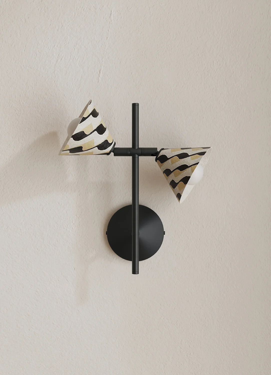 A modern wall-mounted light fixture with a matte black circular base and crossbar, featuring two cone-shaped shades with a black and beige zebra-like pattern, mounted on a textured beige wall.