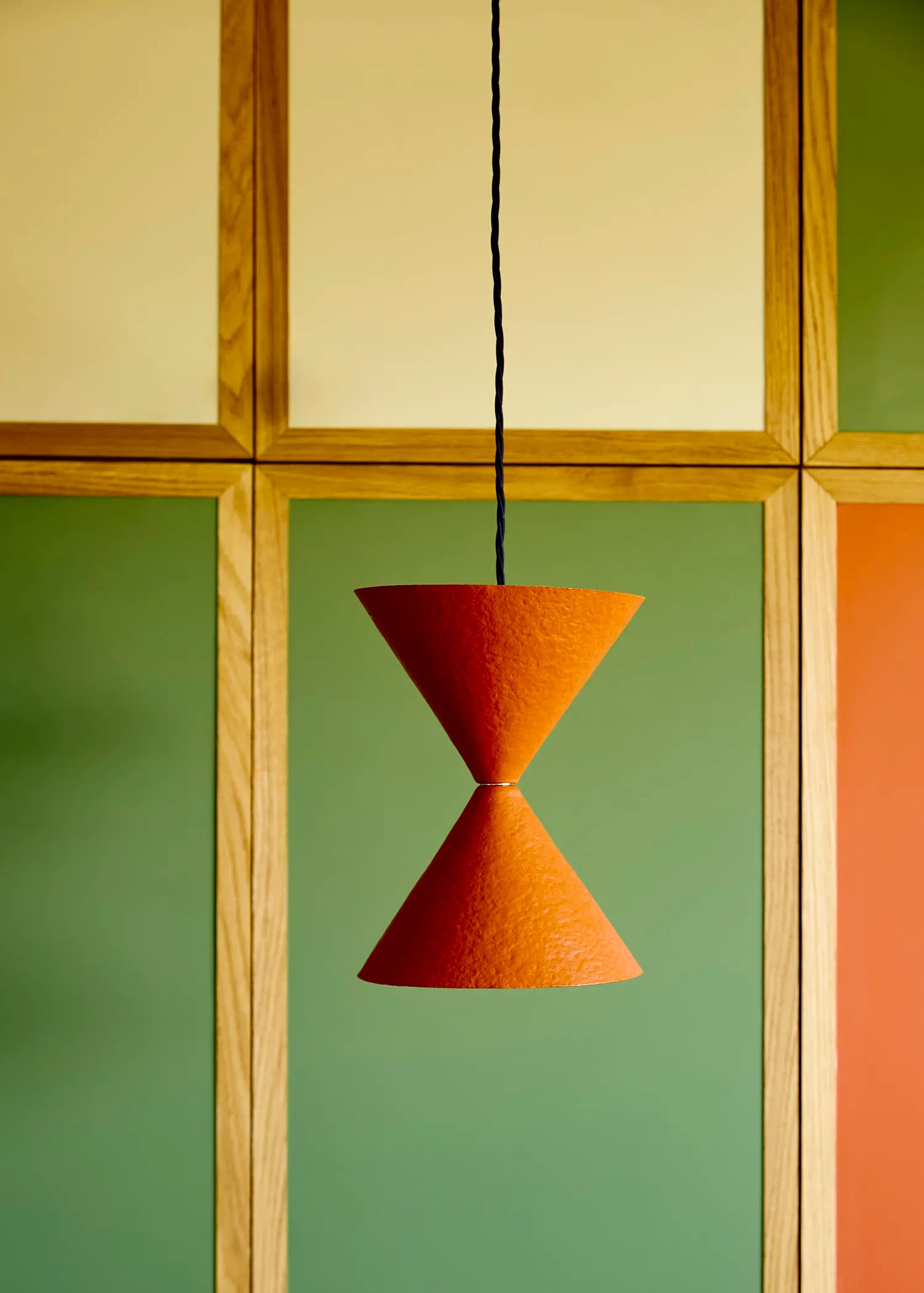 Orange pendant lamp hanging against a geometric wall with wooden and green panels.