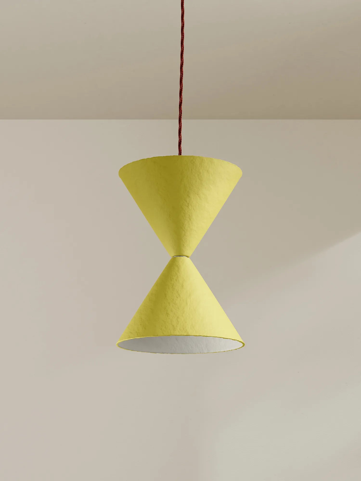 A modern pendant light with two textured yellow cone shades connected at the center, suspended by a burgundy cord against a minimalist beige wall and ceiling.