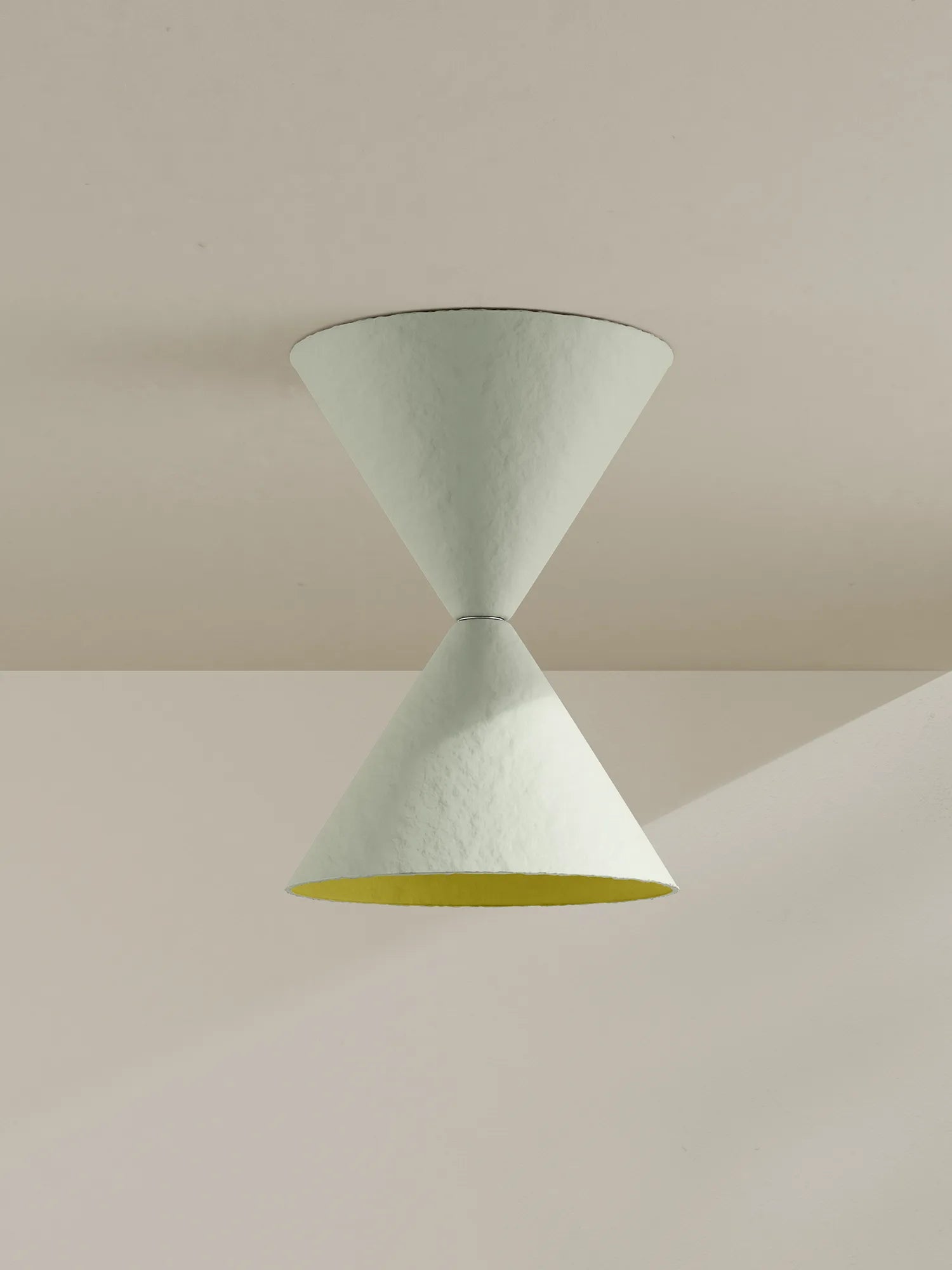 A sculptural two-cone pendant light fixture in a textured off-white finish, featuring a contrasting yellow interior on the lower cone, shown hanging against a minimalist beige wall and ceiling.
