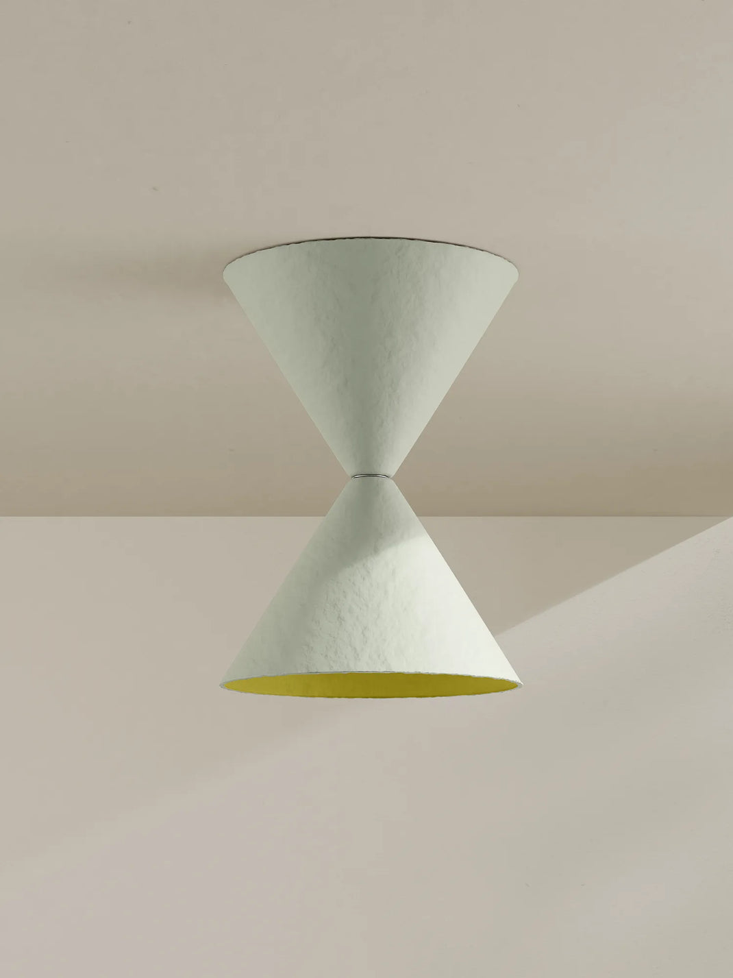 A sculptural two-cone pendant light fixture in a textured off-white finish, featuring a contrasting yellow interior on the lower cone, shown hanging against a minimalist beige wall and ceiling.