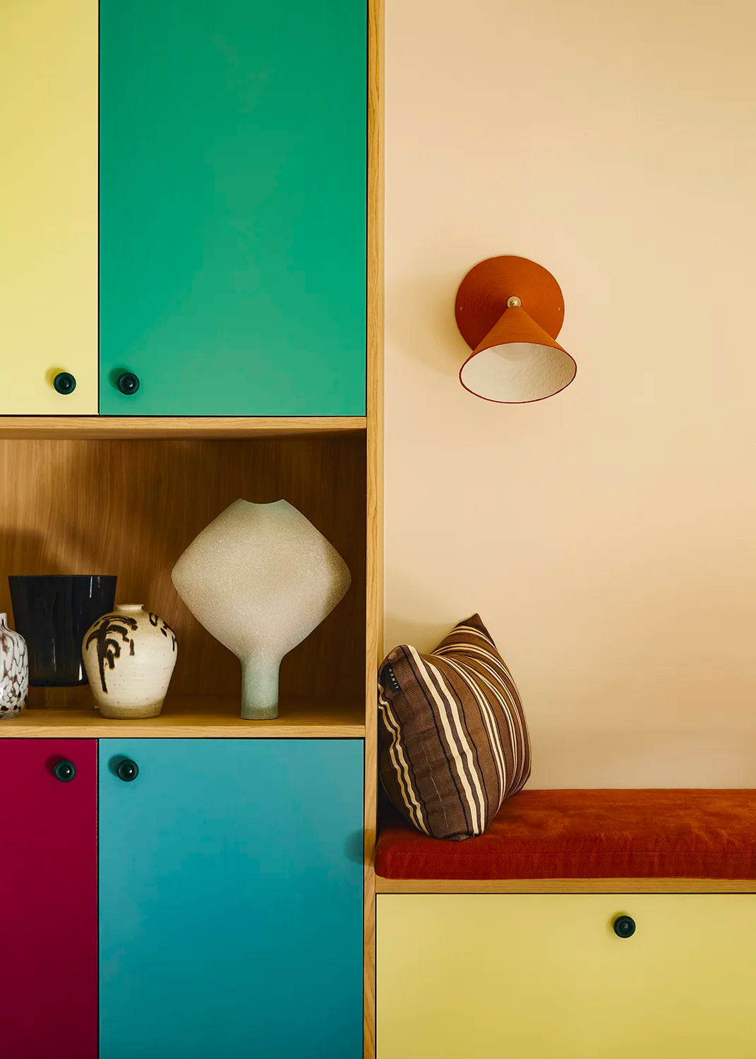 Colorful cabinet with decorative items and a wall lamp in a room setting.