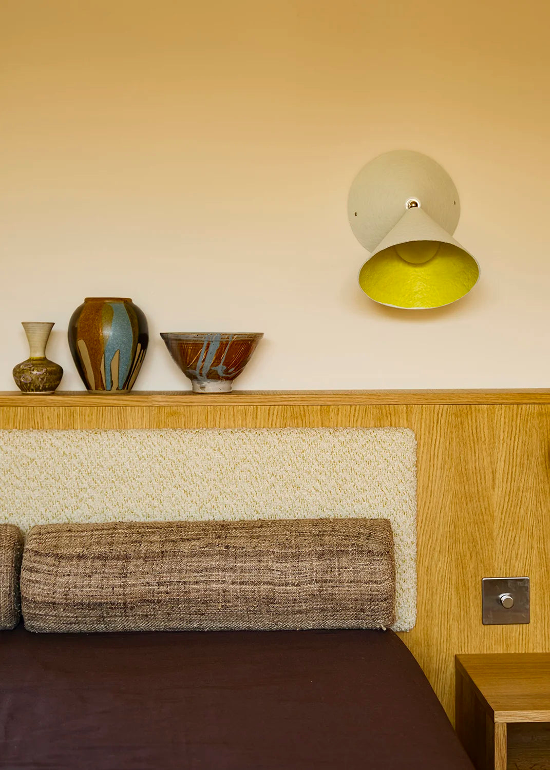 Decorative wall shelf with vases and a lamp above a bed in a bedroom setting.
