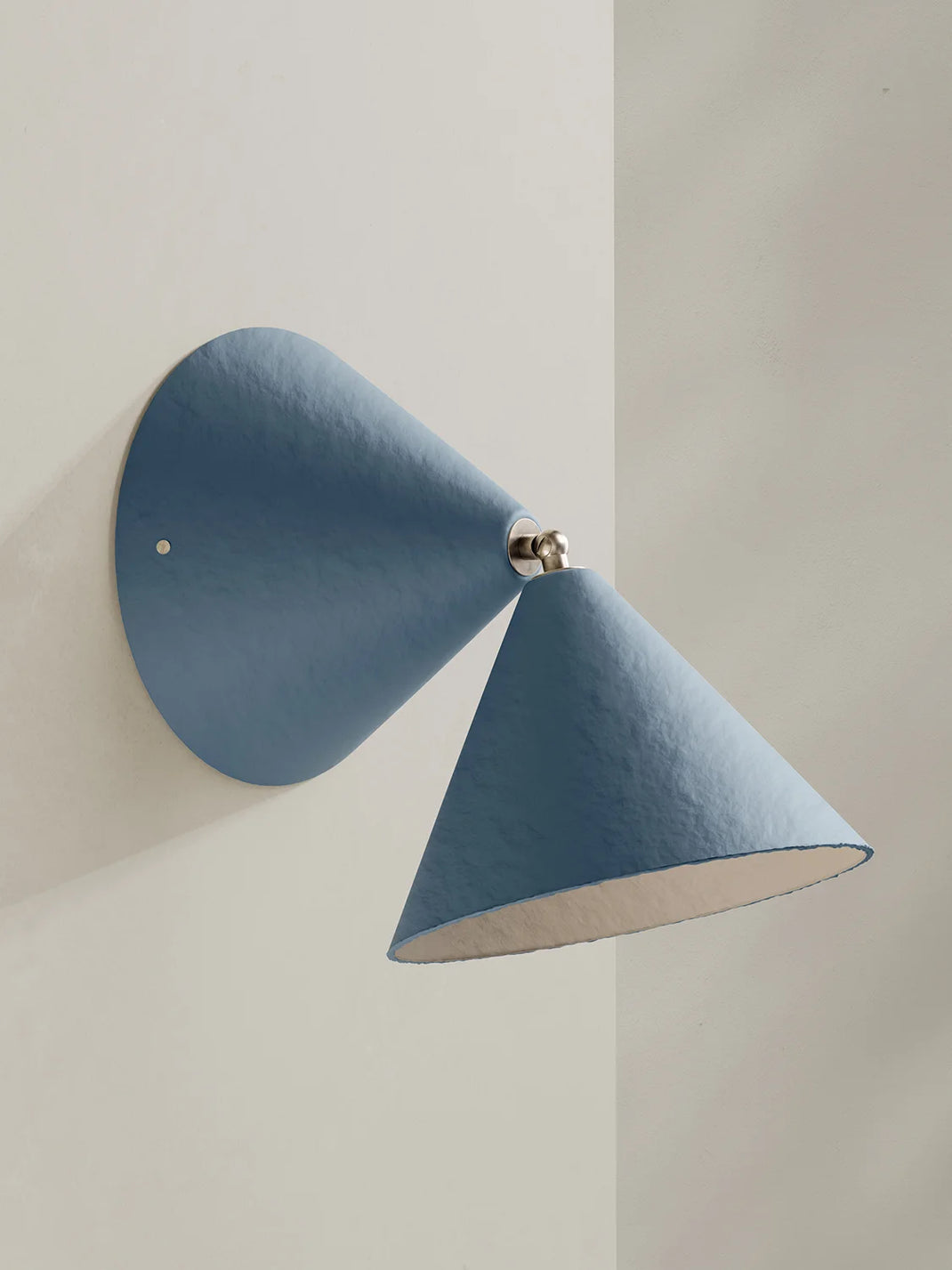 A modern blue wall sconce with a conical shade and a circular backplate, mounted on a light beige wall.