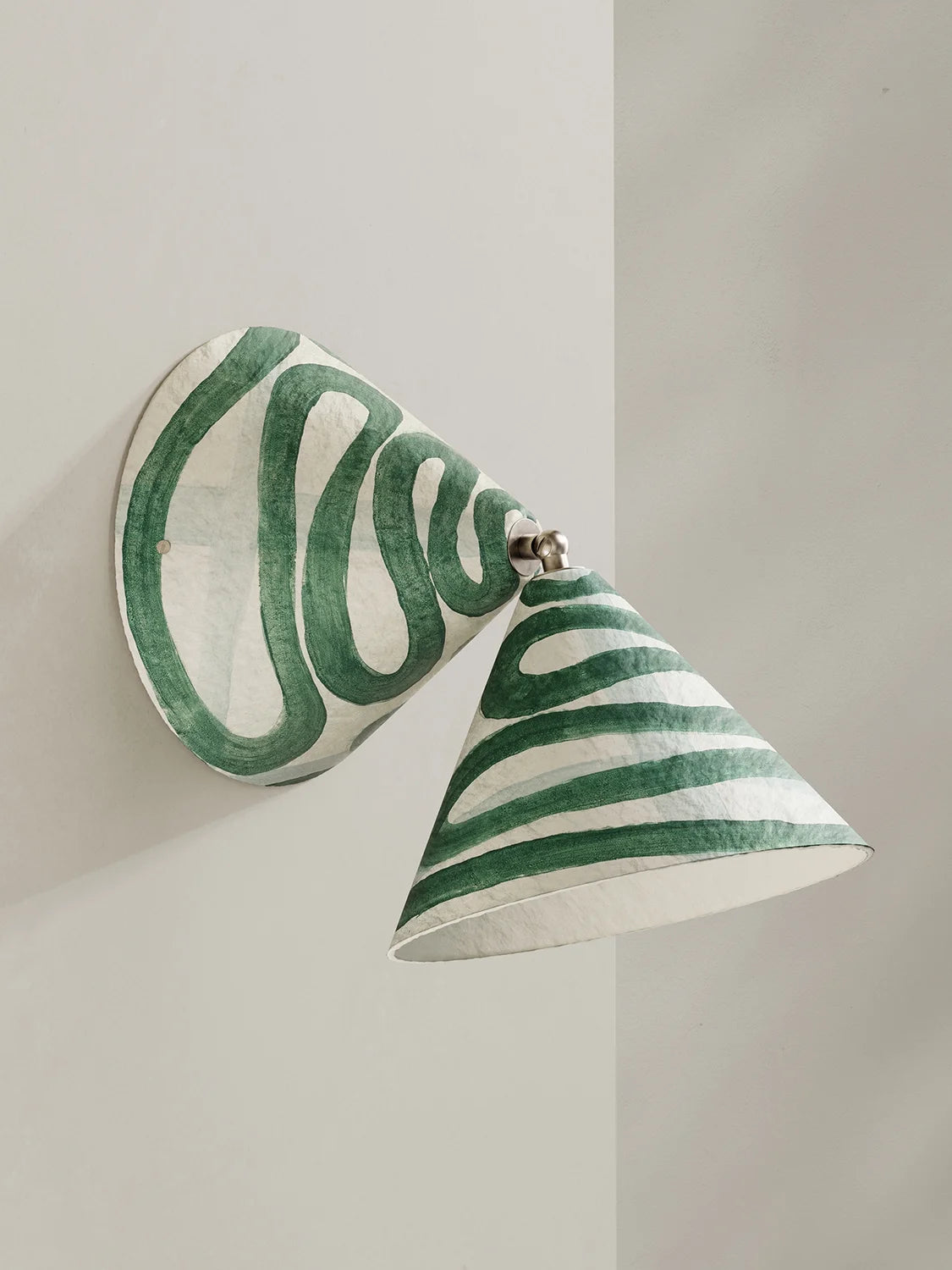 A sculptural wall sconce with a conical shade and round backplate, decorated with hand-painted green and white wavy stripes, mounted on a light gray wall.