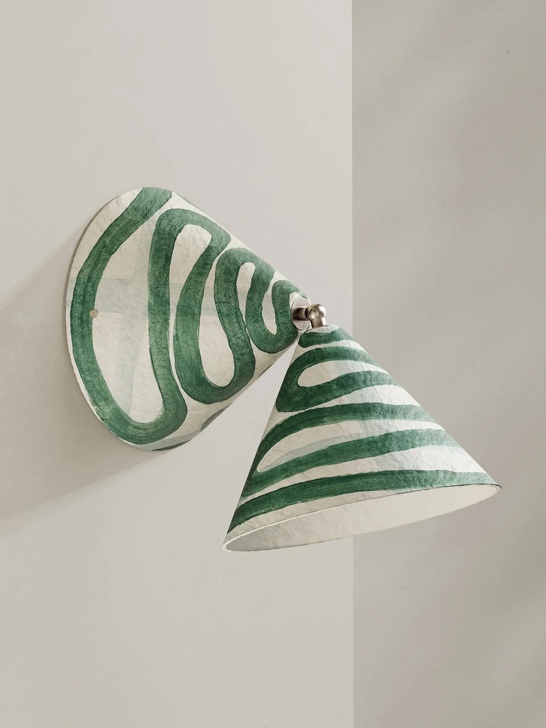 A sculptural wall sconce with a conical shade and round backplate, decorated with hand-painted green and white wavy stripes, mounted on a light gray wall.