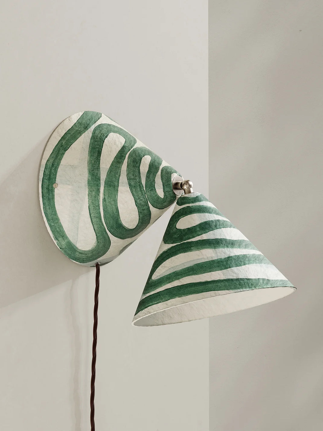 A sculptural wall sconce with a conical shade, decorated with hand-painted green and white swirl, mounted on a light gray wall.