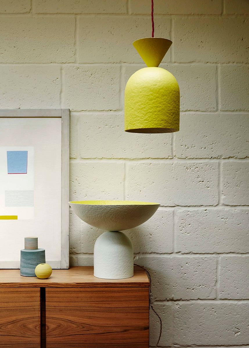 White table lamp on a sideboard with a yellow pendant hanging from above