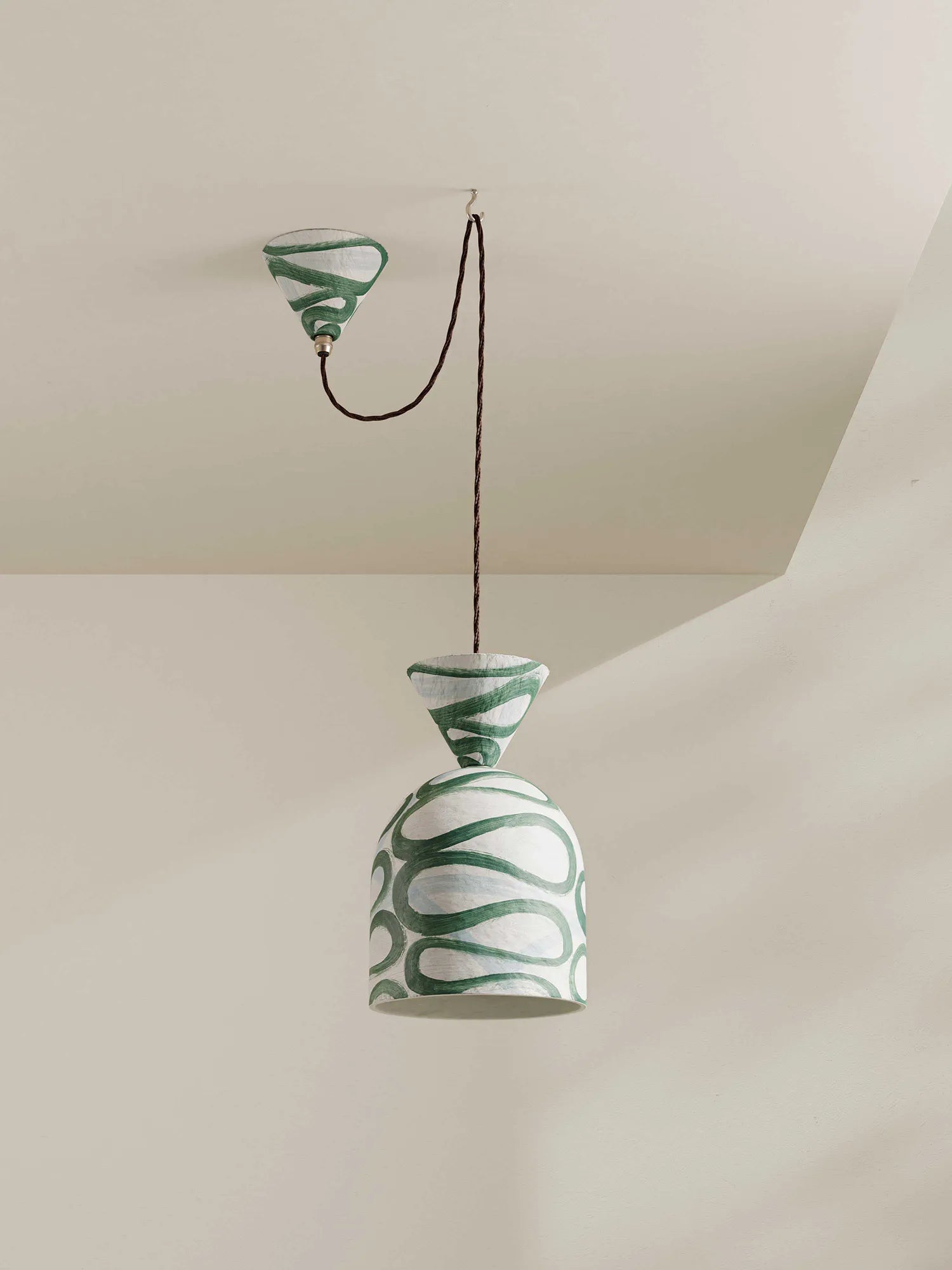 A paper-pulp pendant light with a white and green pattern, suspended from a ceiling by a brown cord.