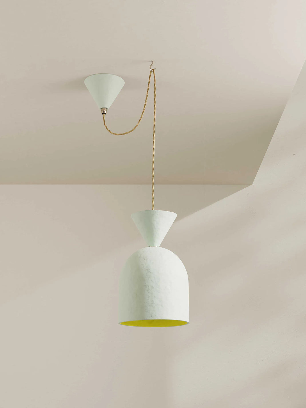 A modern pendant light with a textured white dome shade, a conical white ceiling mount, and a beige-toned hanging cord, shown installed against a minimalist neutral wall and ceiling.