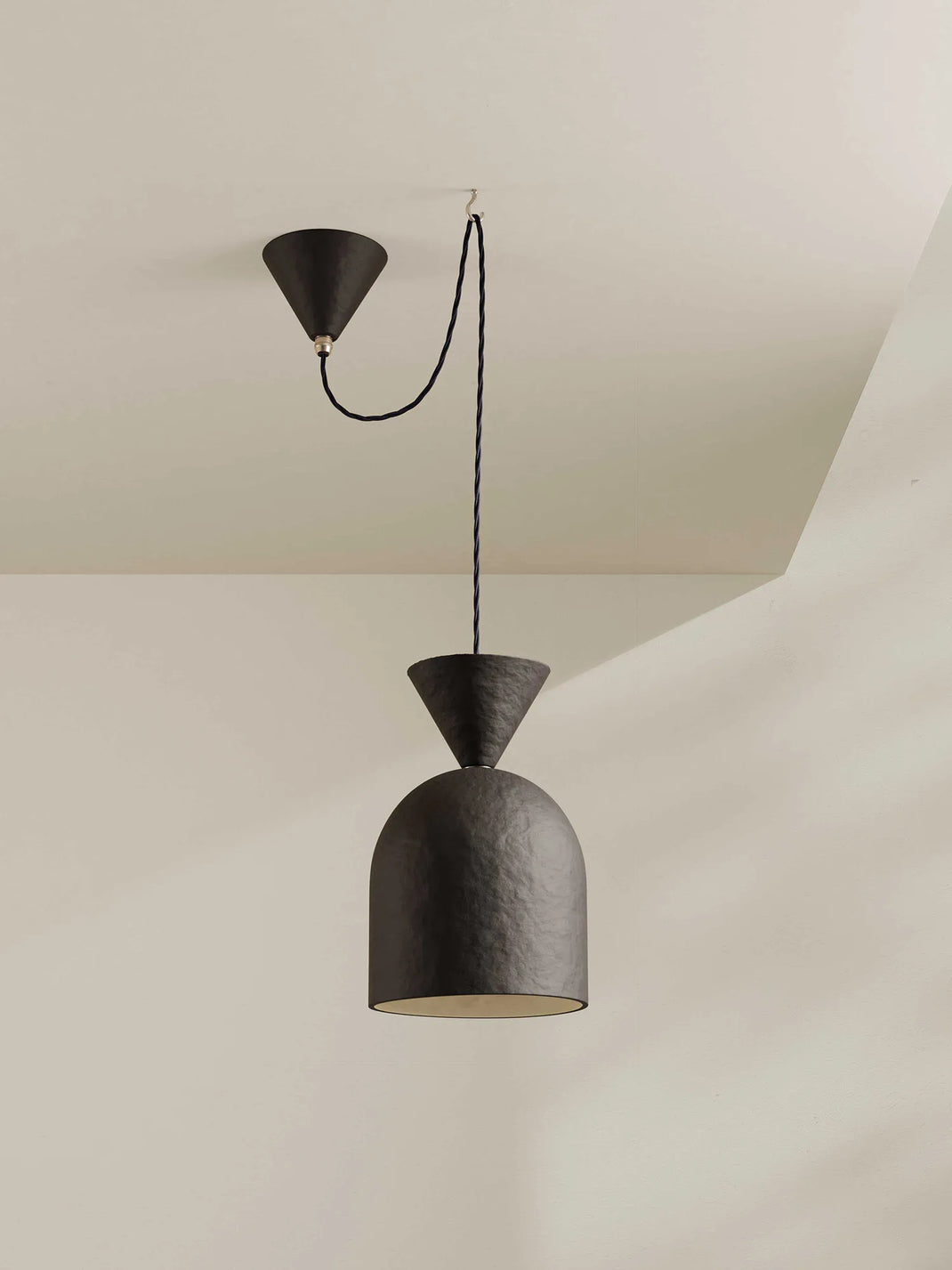 A bell-shaped pendant light in dark-brown with a midnight blue cord hangs against a neutral background