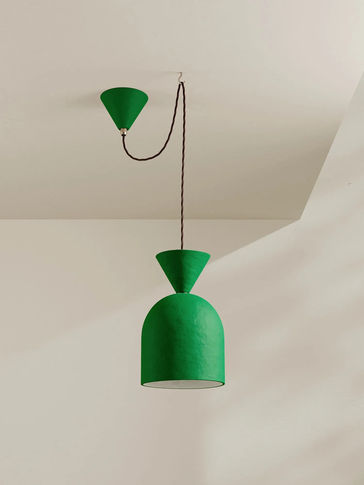 A green pendant light with a textured green shade and a matching green ceiling canopy, suspended by a brown cord against a warm off-white wall and ceiling.