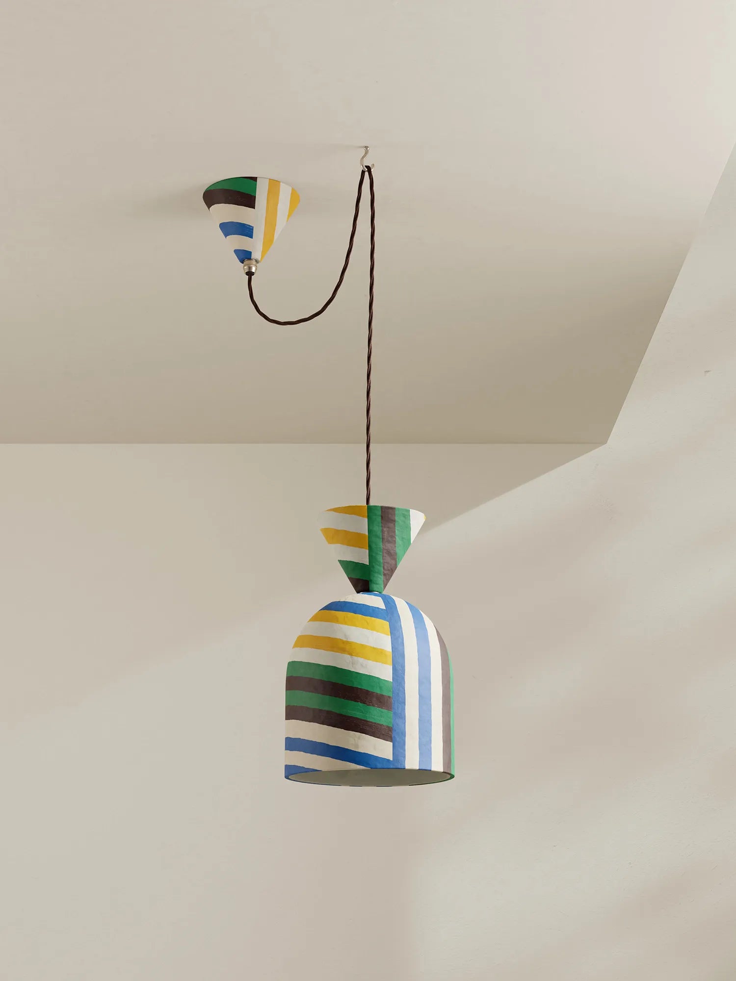 A colorful pendant light with a striped bell-shaped shade hanging from a brown cord and matching striped ceiling canopy, shown against a plain off-white wall and ceiling.