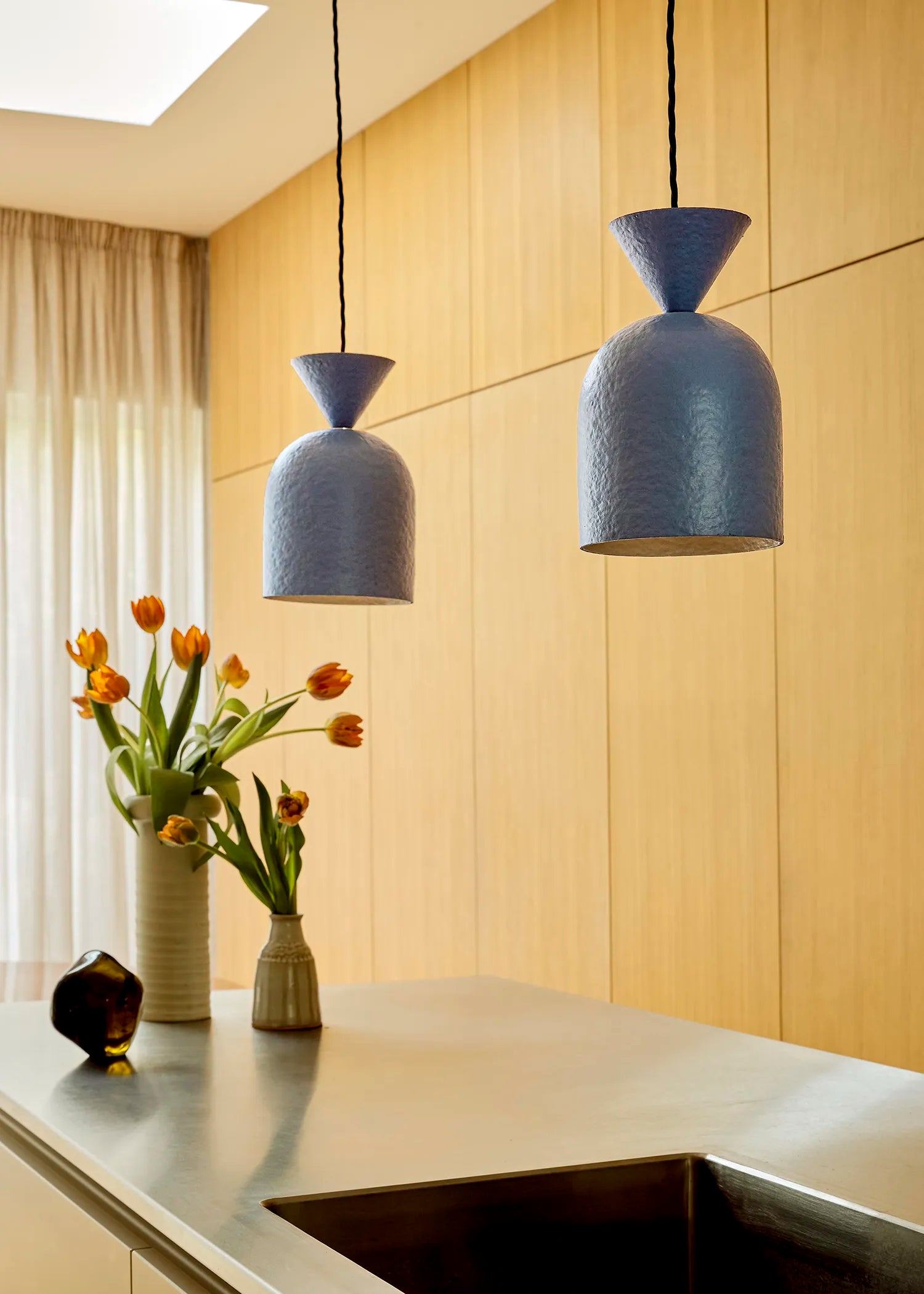 Blue pendant lights hanging above a kitchen counter with a vase of flowers and a light fixture.